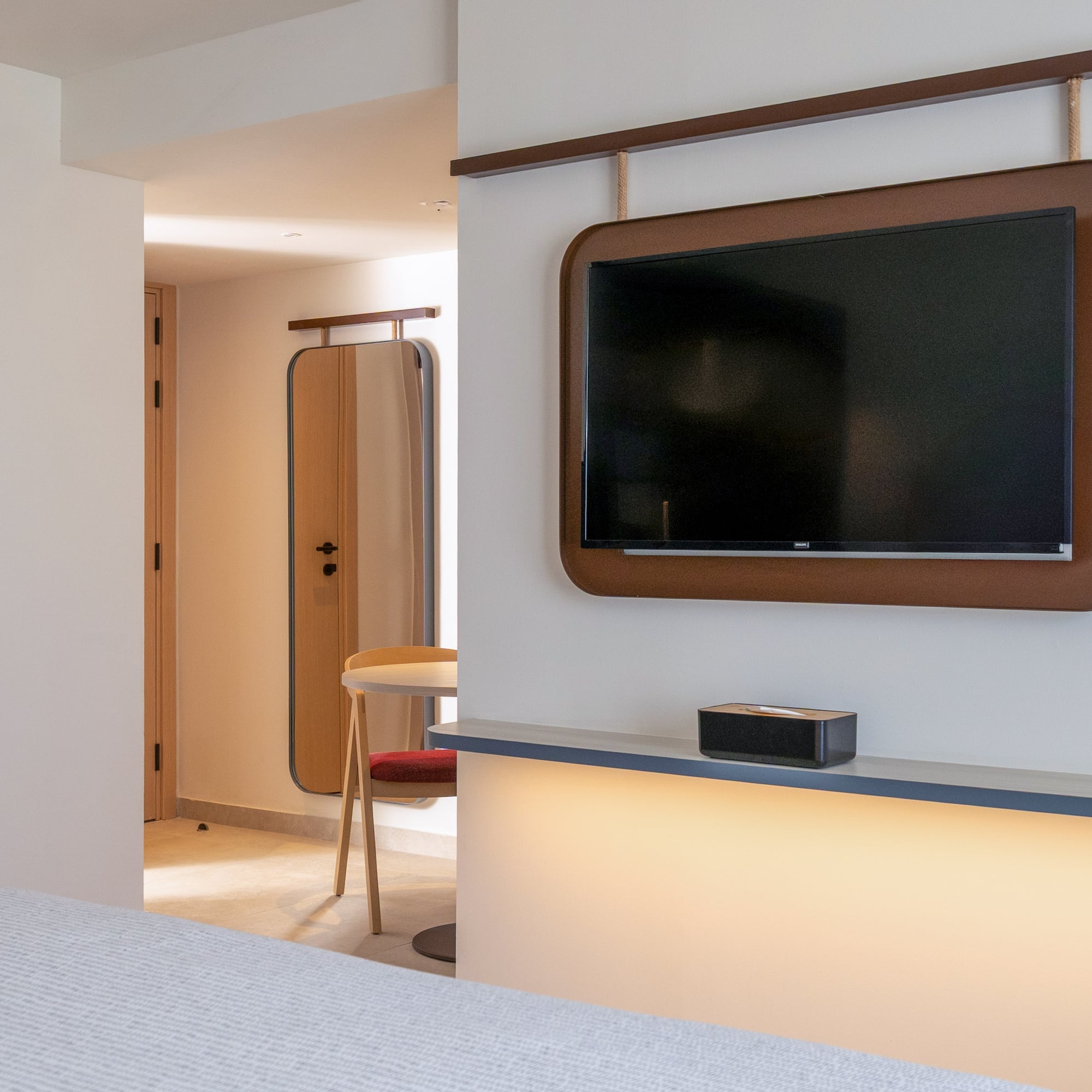 Modern hotel room with wall-mounted TV, brown frame, and illuminated shelf.
