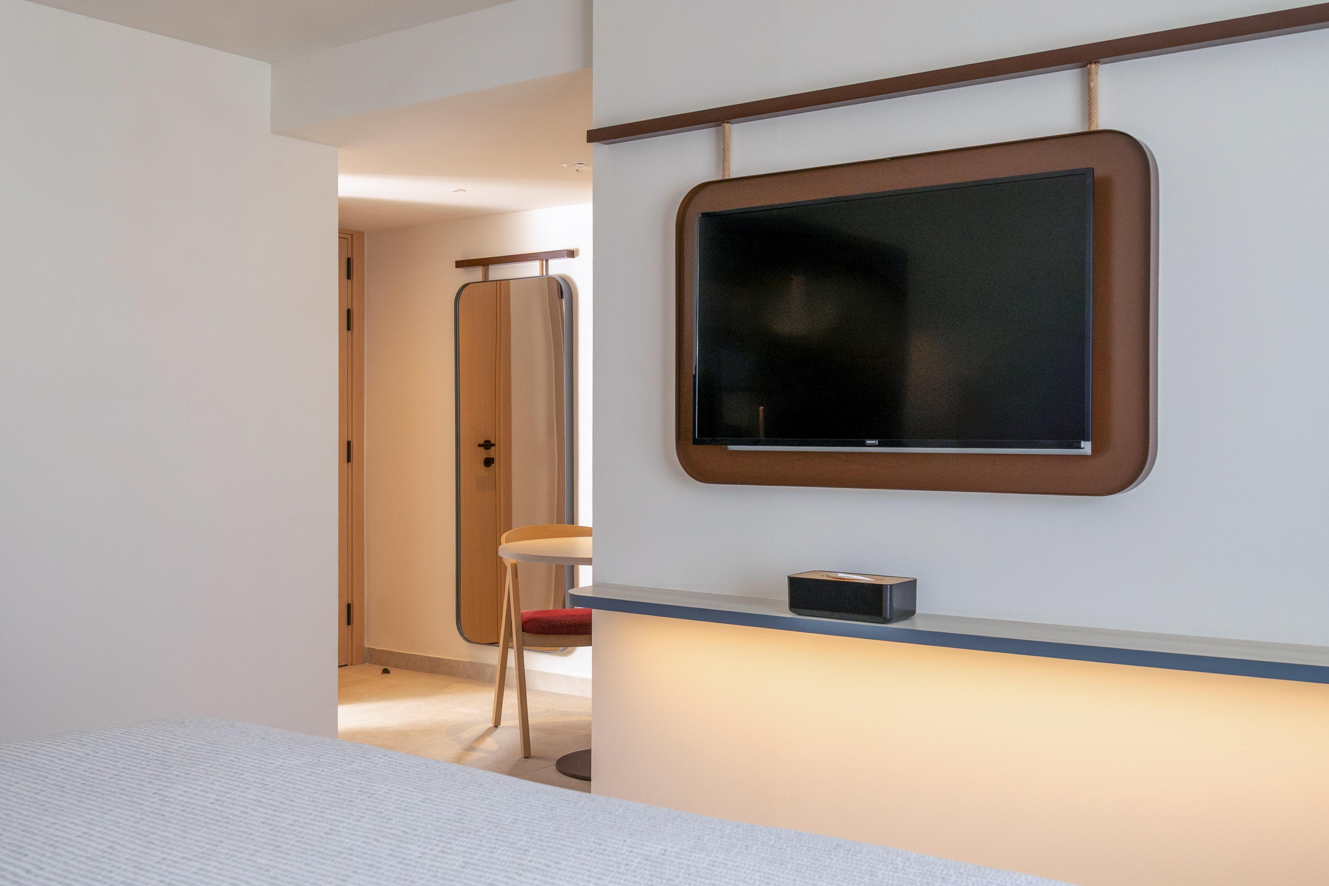 Modern hotel room with wall-mounted TV, brown frame, and illuminated shelf.