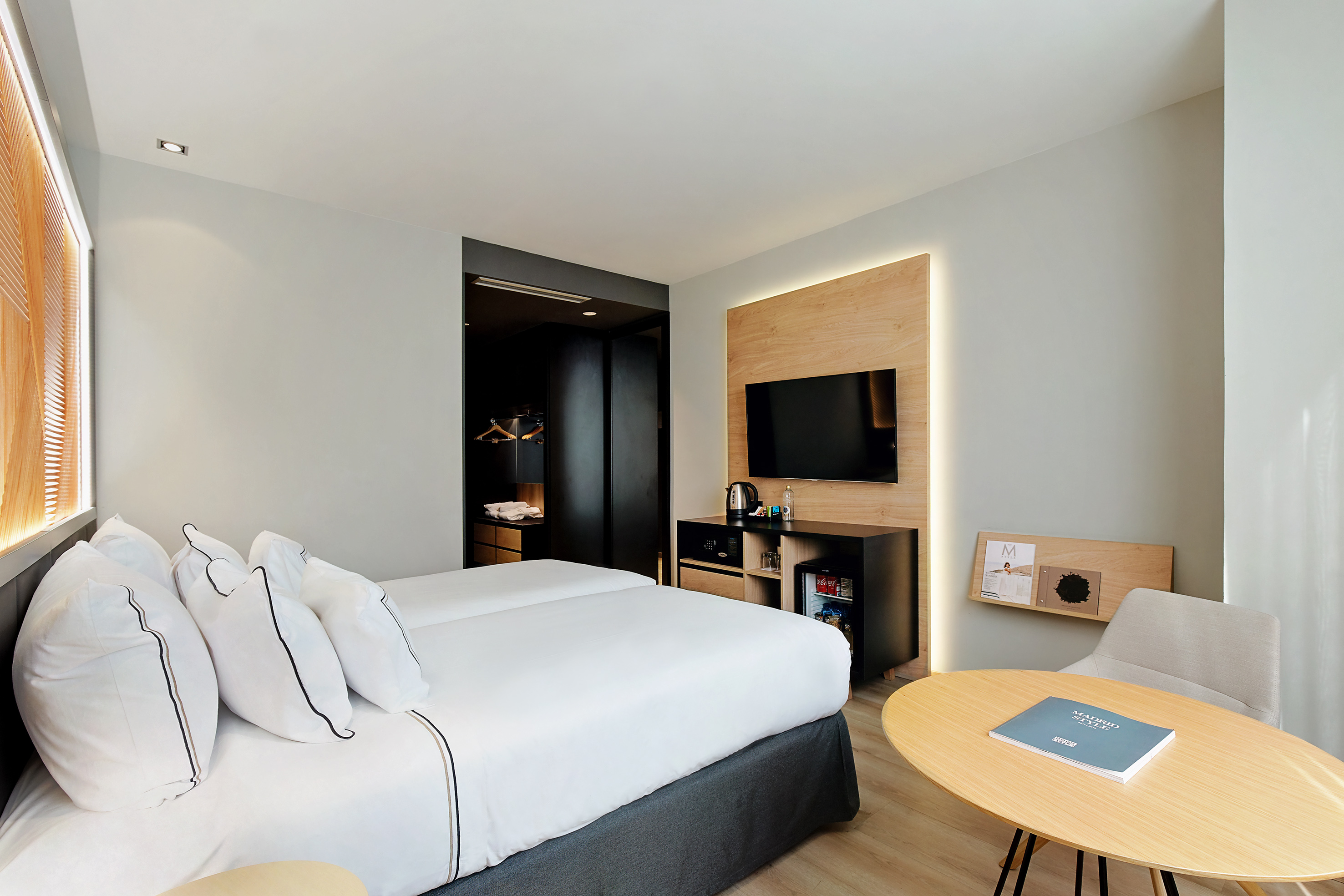Modern hotel bedroom with two beds, TV, mini-fridge, and stylish wood accents.