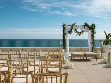 a wedding set up on a patio with chairs and a large body of water