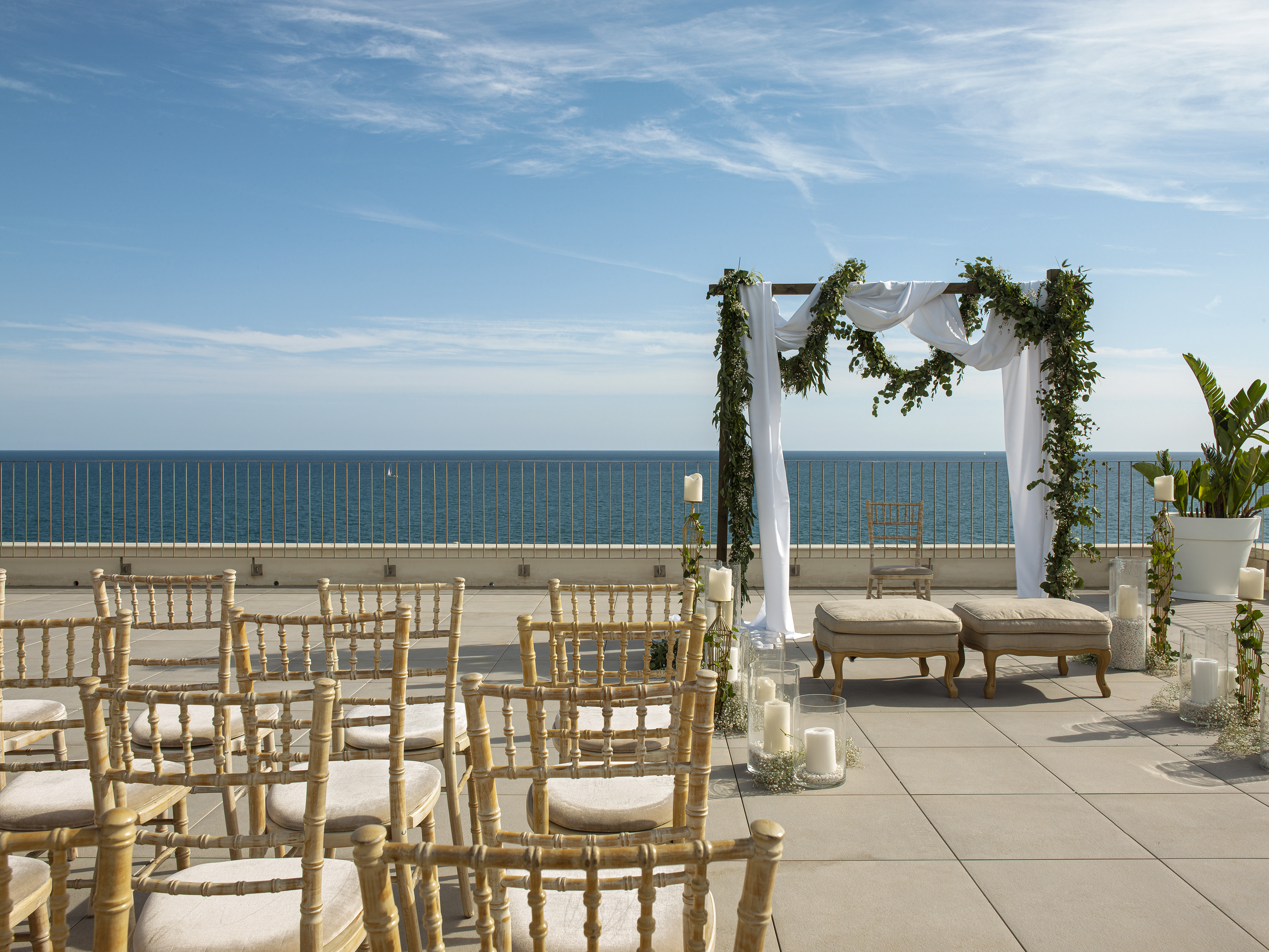 Rooftop ocean view wedding ceremony with decorated arch and chairs.