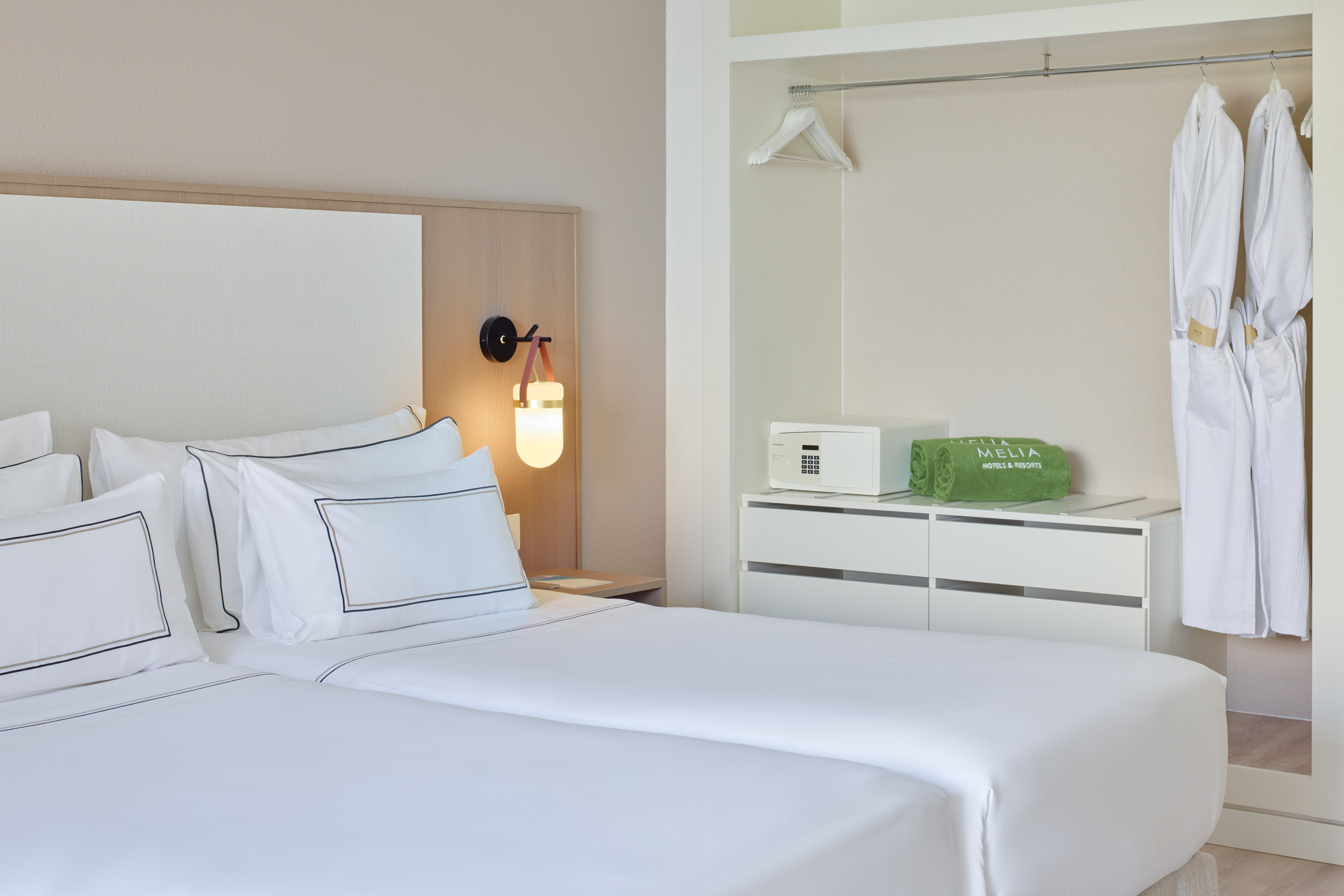 Melia hotel room with two beds, modern lamp, wardrobe, bathrobes, and safe.