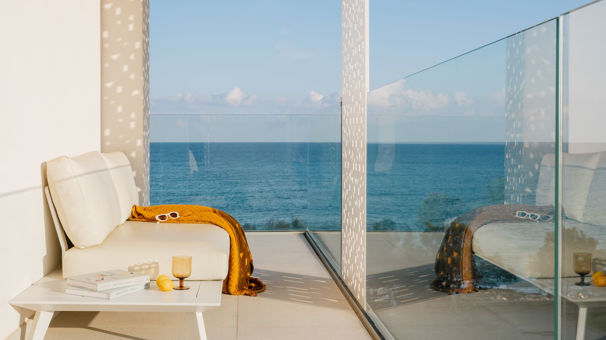 Modern balcony with white outdoor sofa, yellow throw, and ocean view.