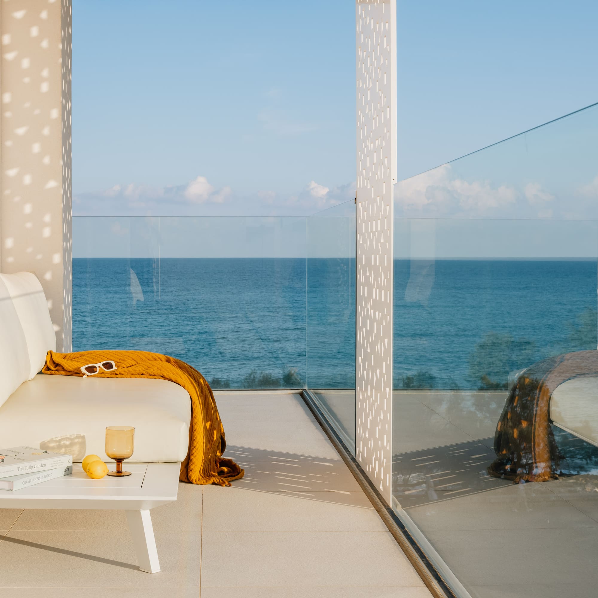 Modern balcony with white outdoor sofa, yellow throw, and ocean view.
