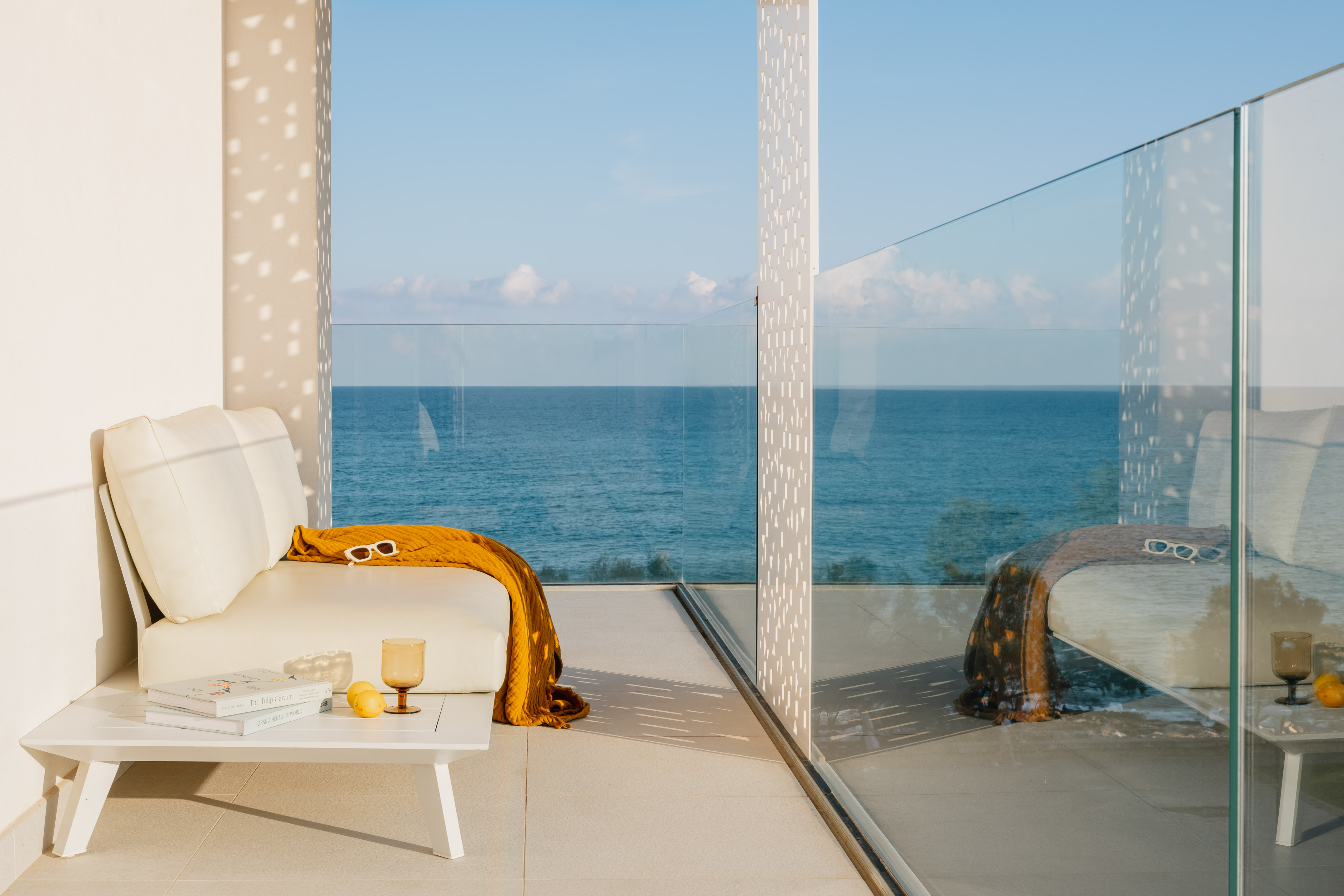 Modern balcony with white outdoor sofa, yellow throw, and ocean view.