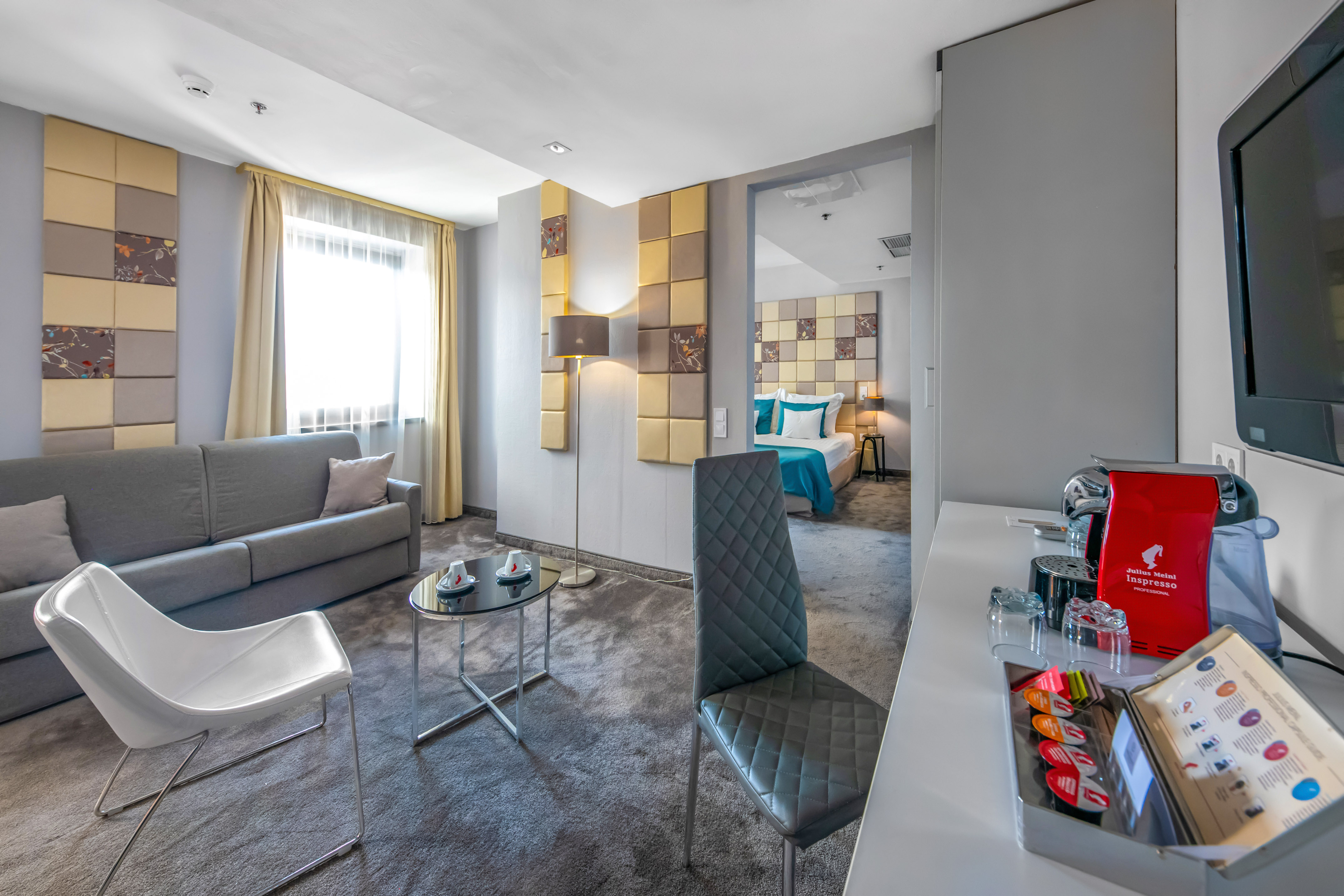 Modern hotel suite with living area, bedroom, and espresso machine.