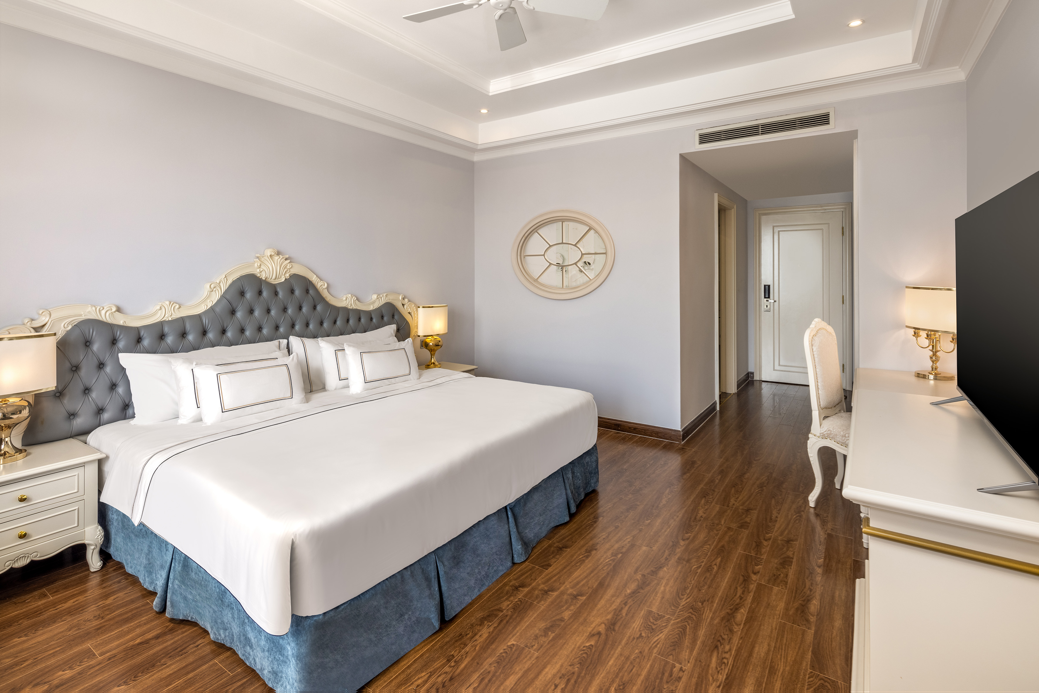Elegant hotel bedroom with king bed, tufted headboard, and polished wood floor.
