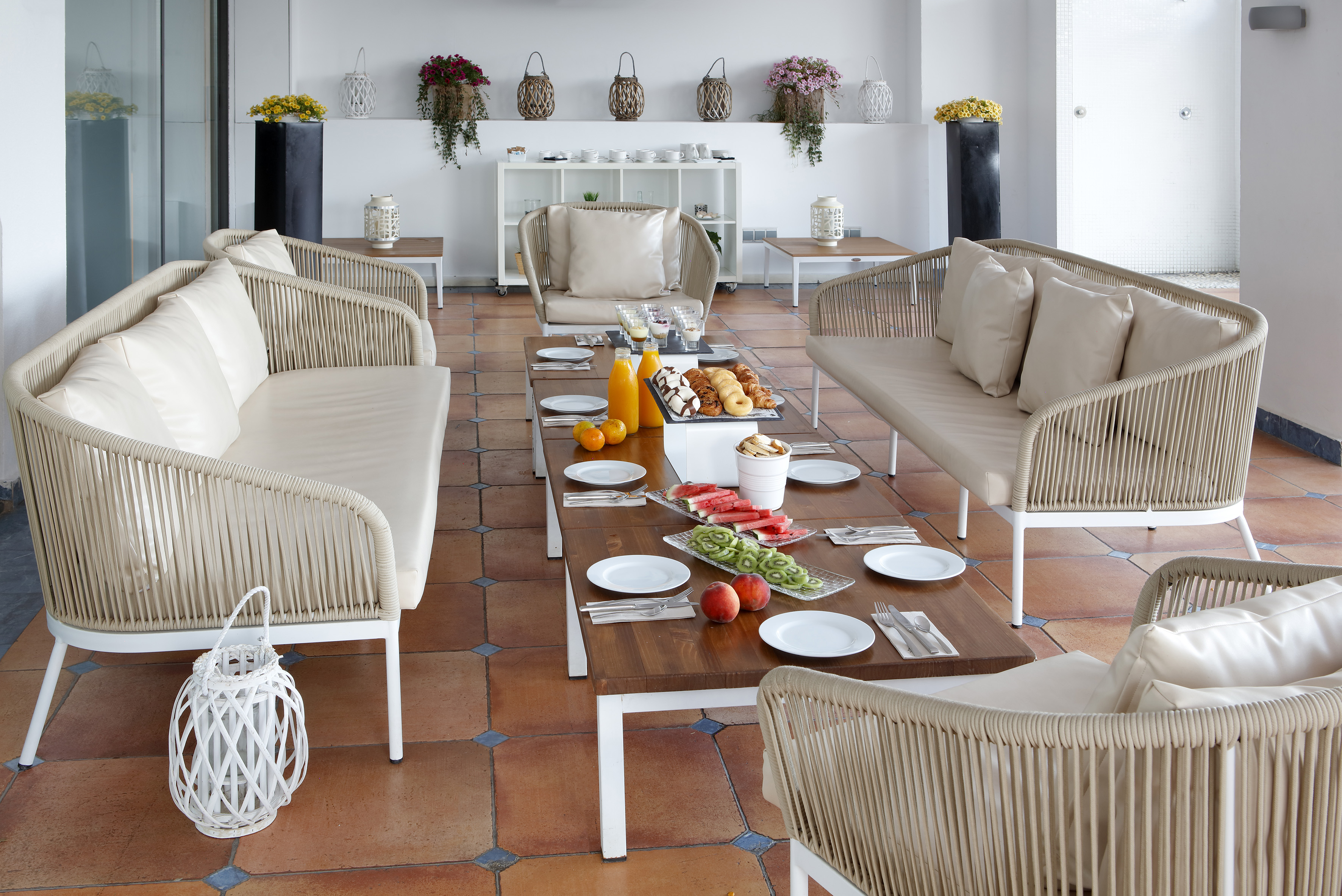 Patio breakfast buffet with rattan seating, fresh fruit, and pastries.