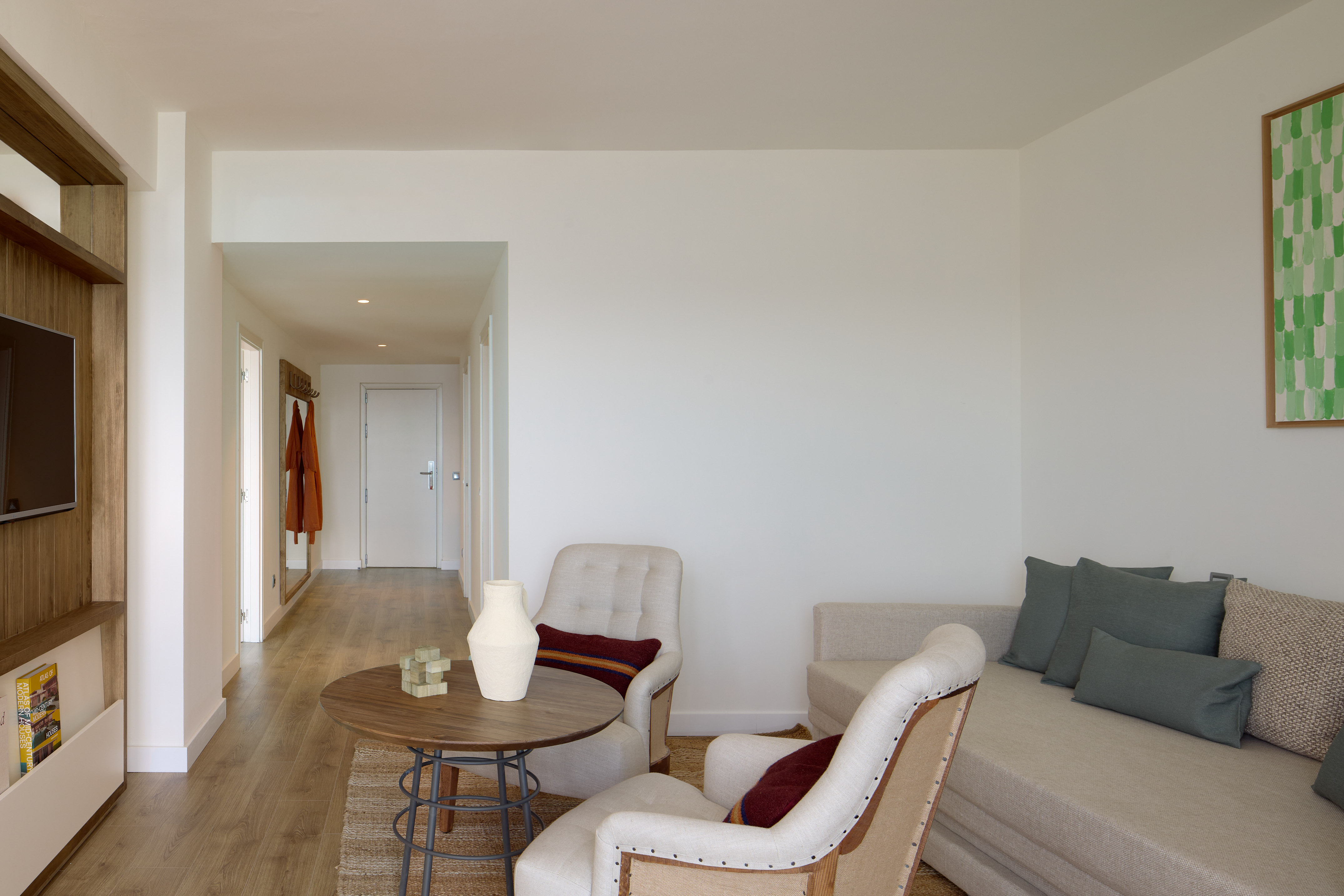 Modern hotel suite living room with light decor, armchairs, sofa, and wood flooring.