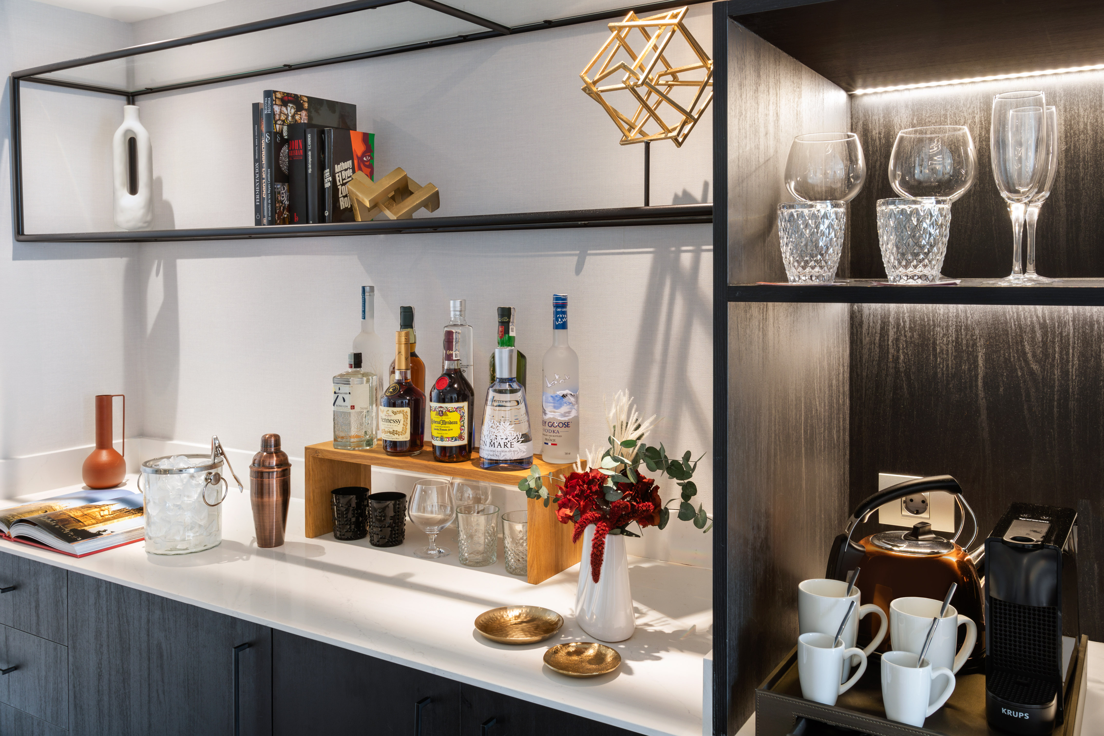 Hotel mini-bar with liquor, cocktail shaker, coffee maker, and elegant glassware.