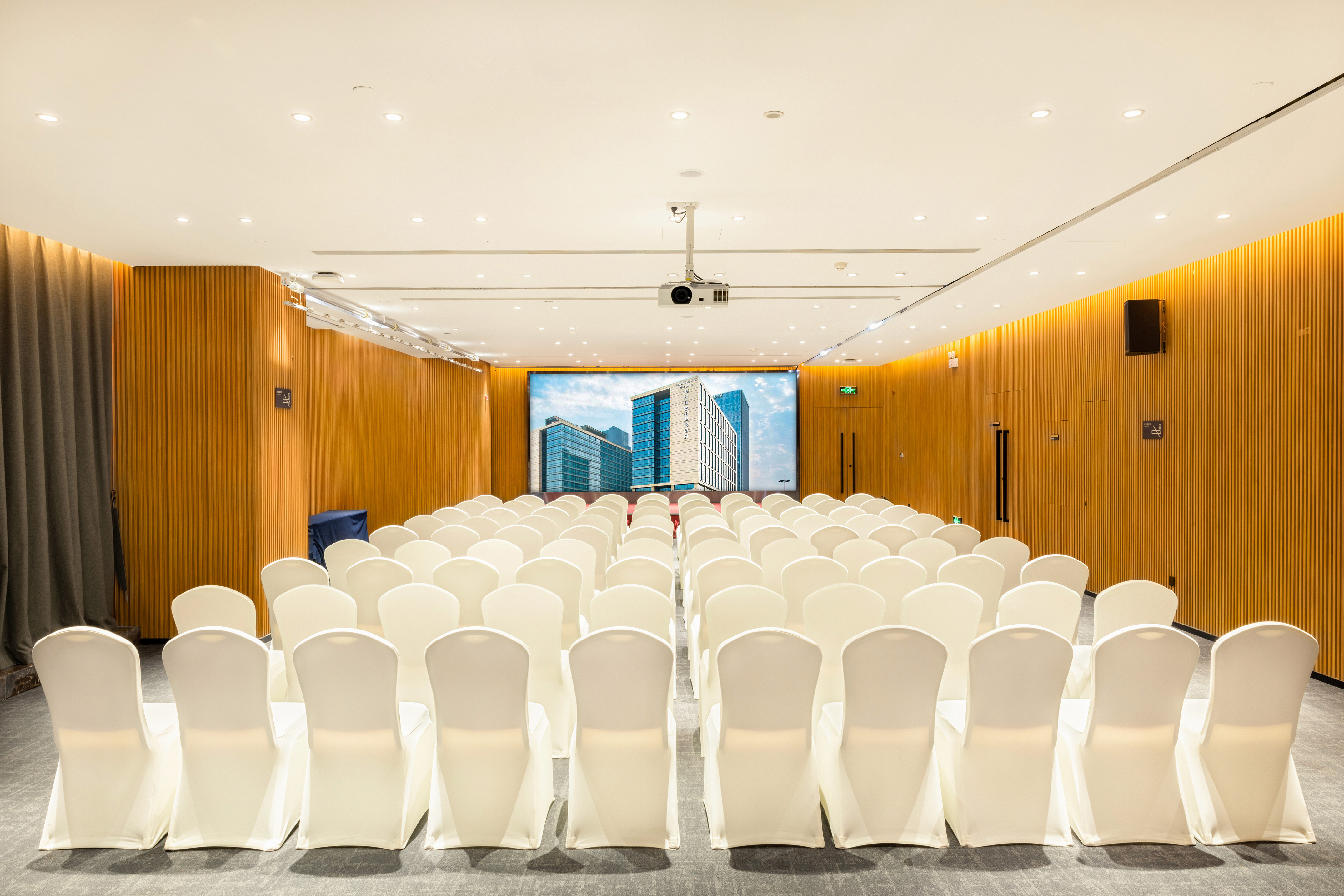 Empty conference room with white chairs, projector screen, wooden walls.