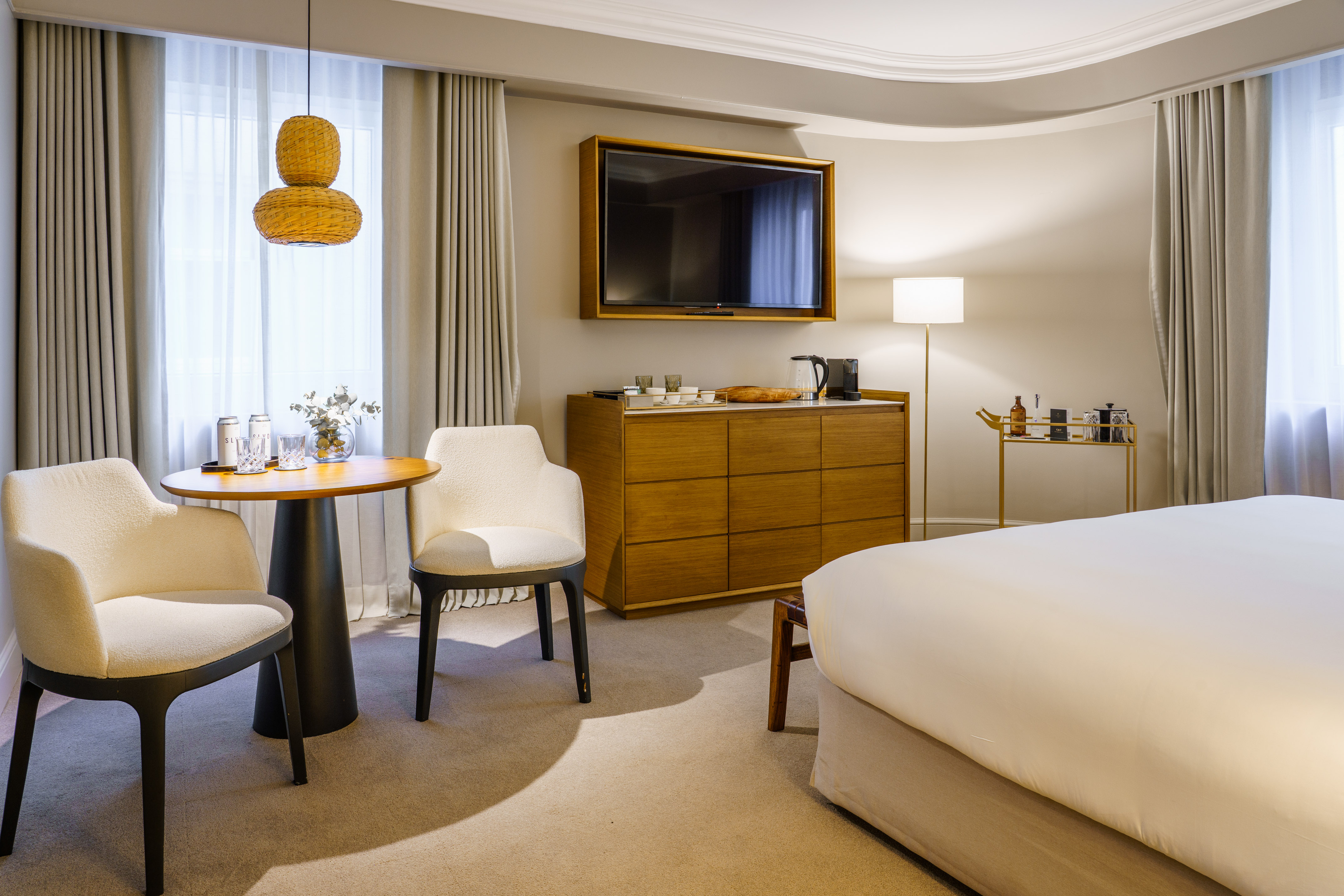 Stylish hotel room featuring a large bed, mounted TV, dresser, and a seating nook.