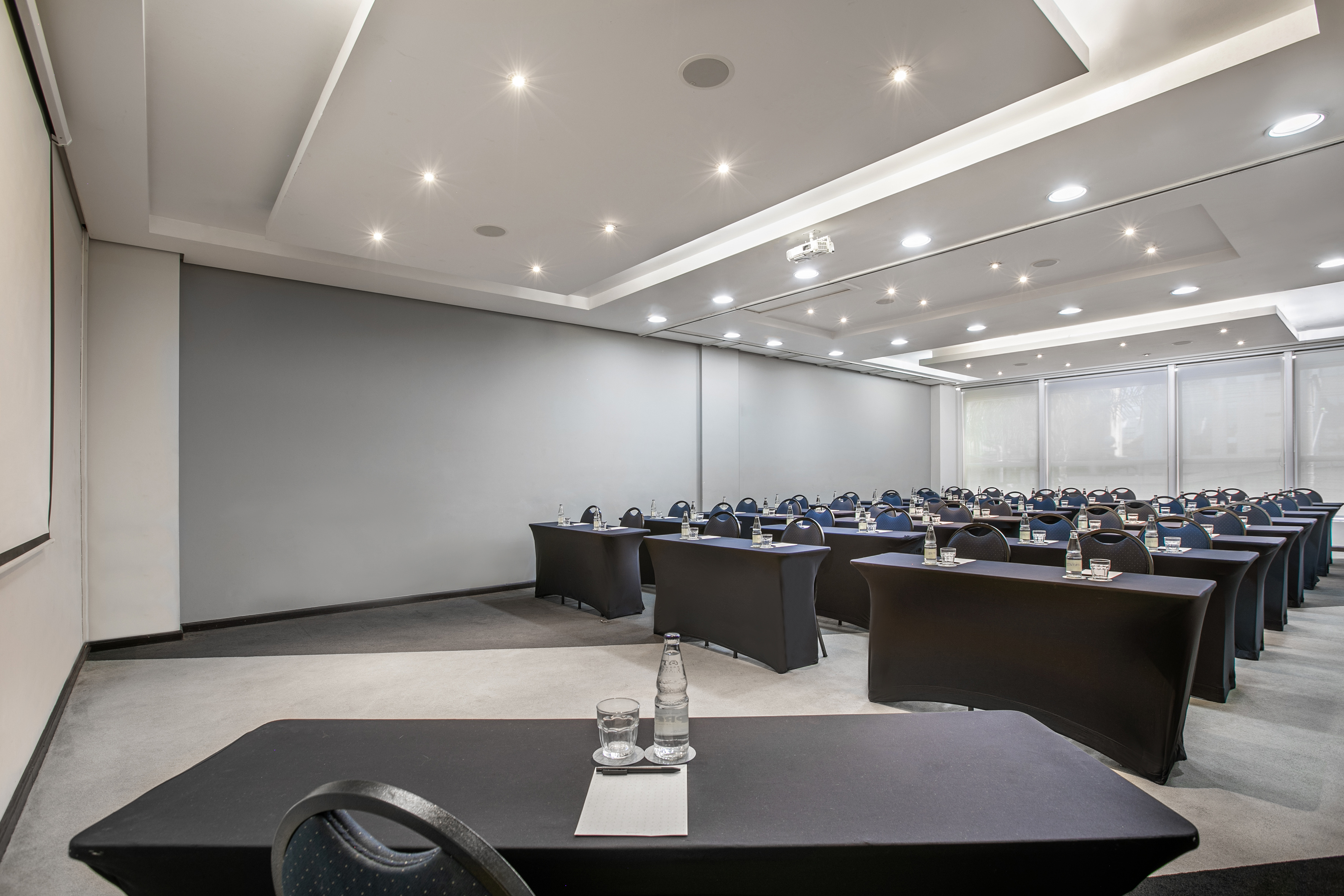 Empty corporate conference room setup with tables, chairs, projector, and screen.