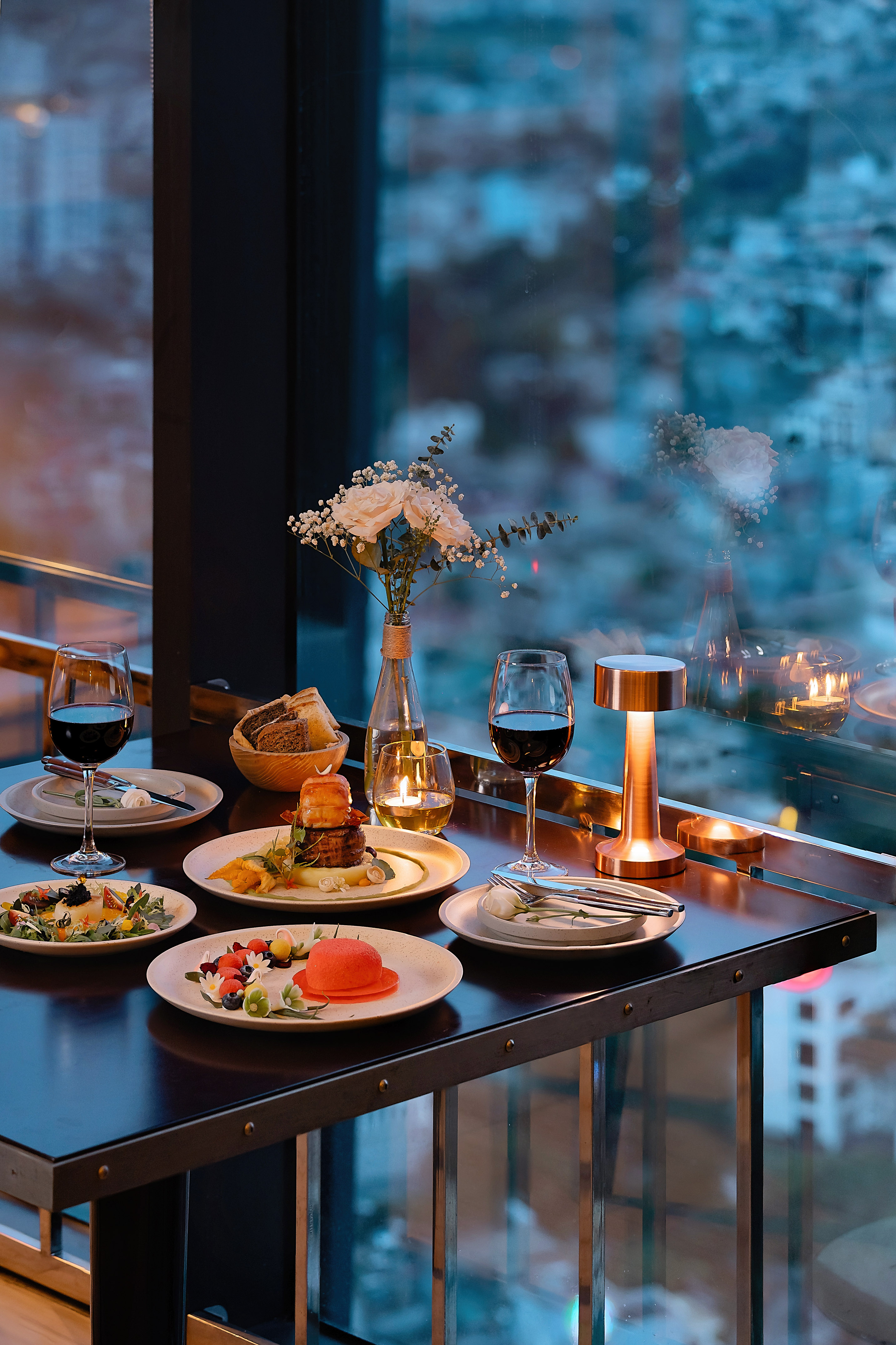 Romantic fine dining dinner with wine and gourmet food by a city window at dusk.