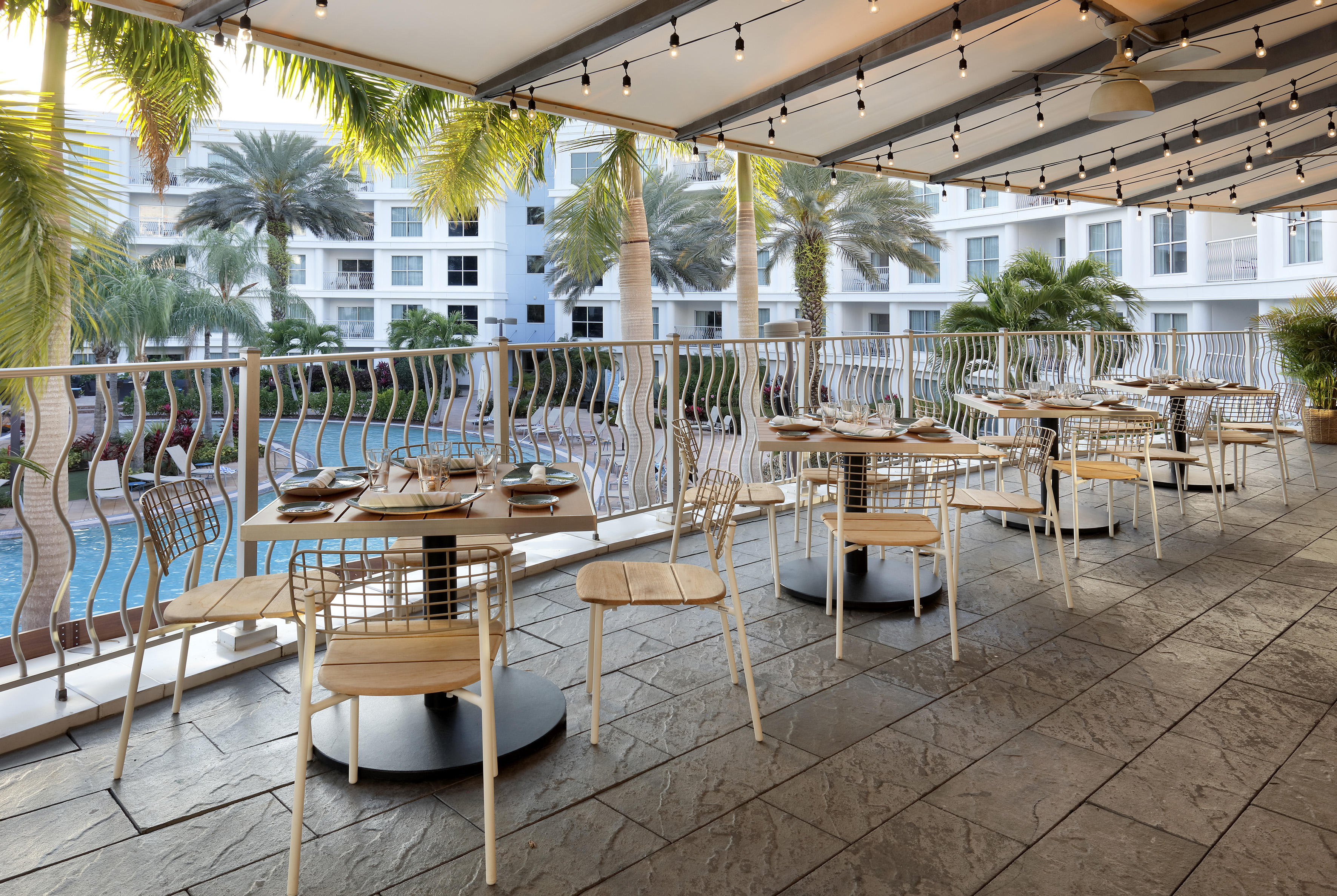 Outdoor resort restaurant patio with set tables, string lights, and pool view. - The Pearl (circular floor plan) - Meliá Orlando Celebration, Orlando