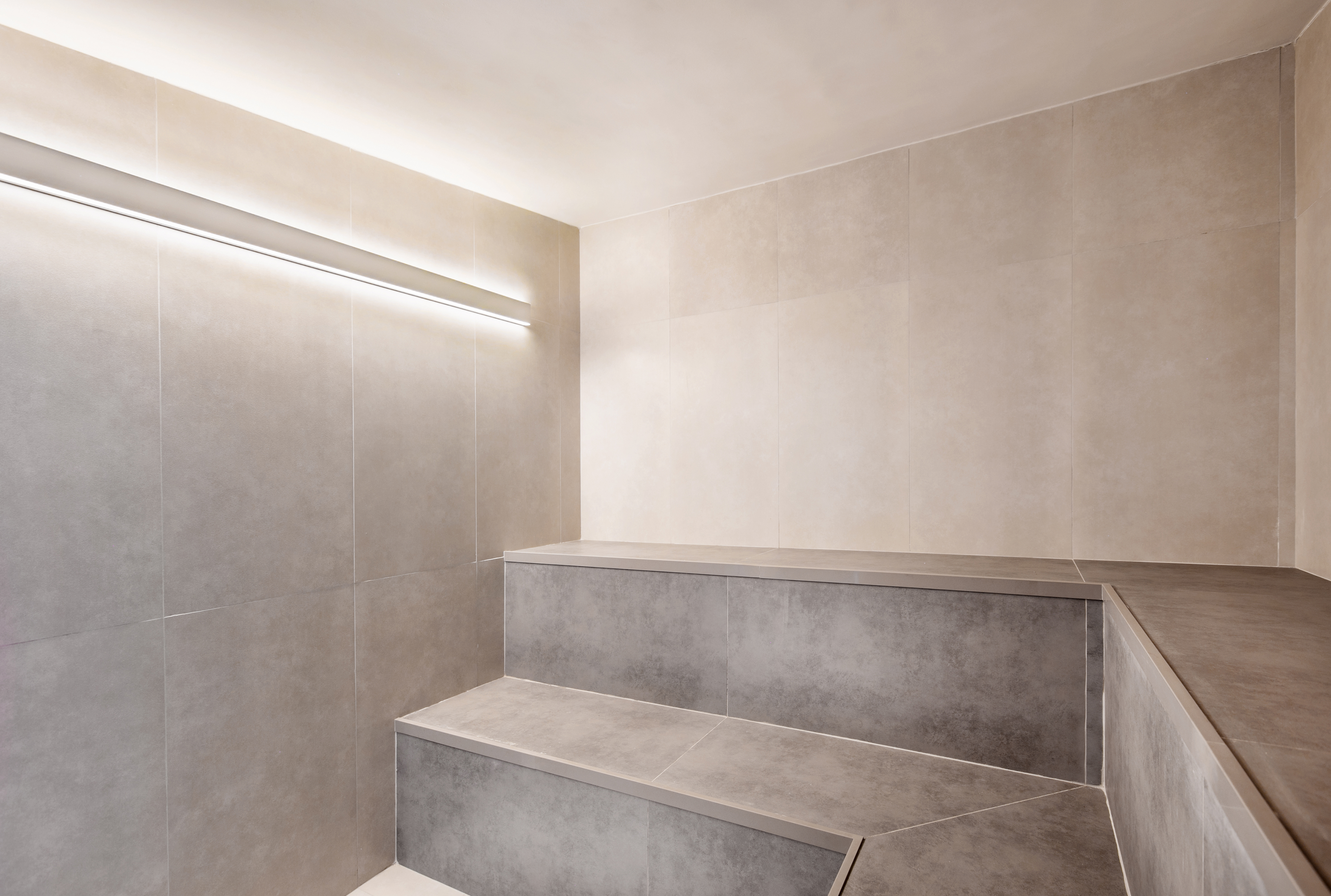 Modern tiled steam room with built-in seating and linear LED light.