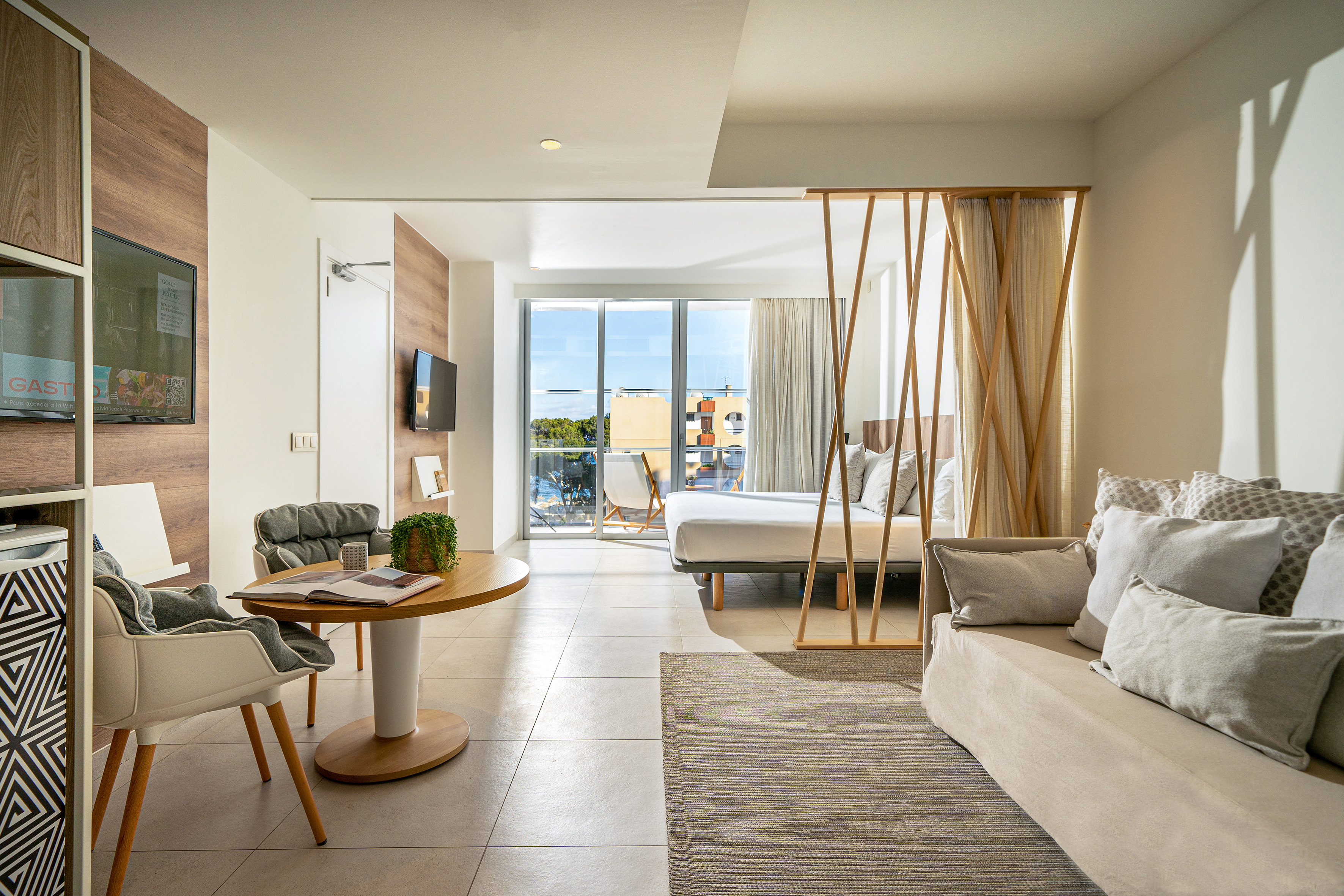 Bright modern hotel suite with living area, bedroom, and balcony view.