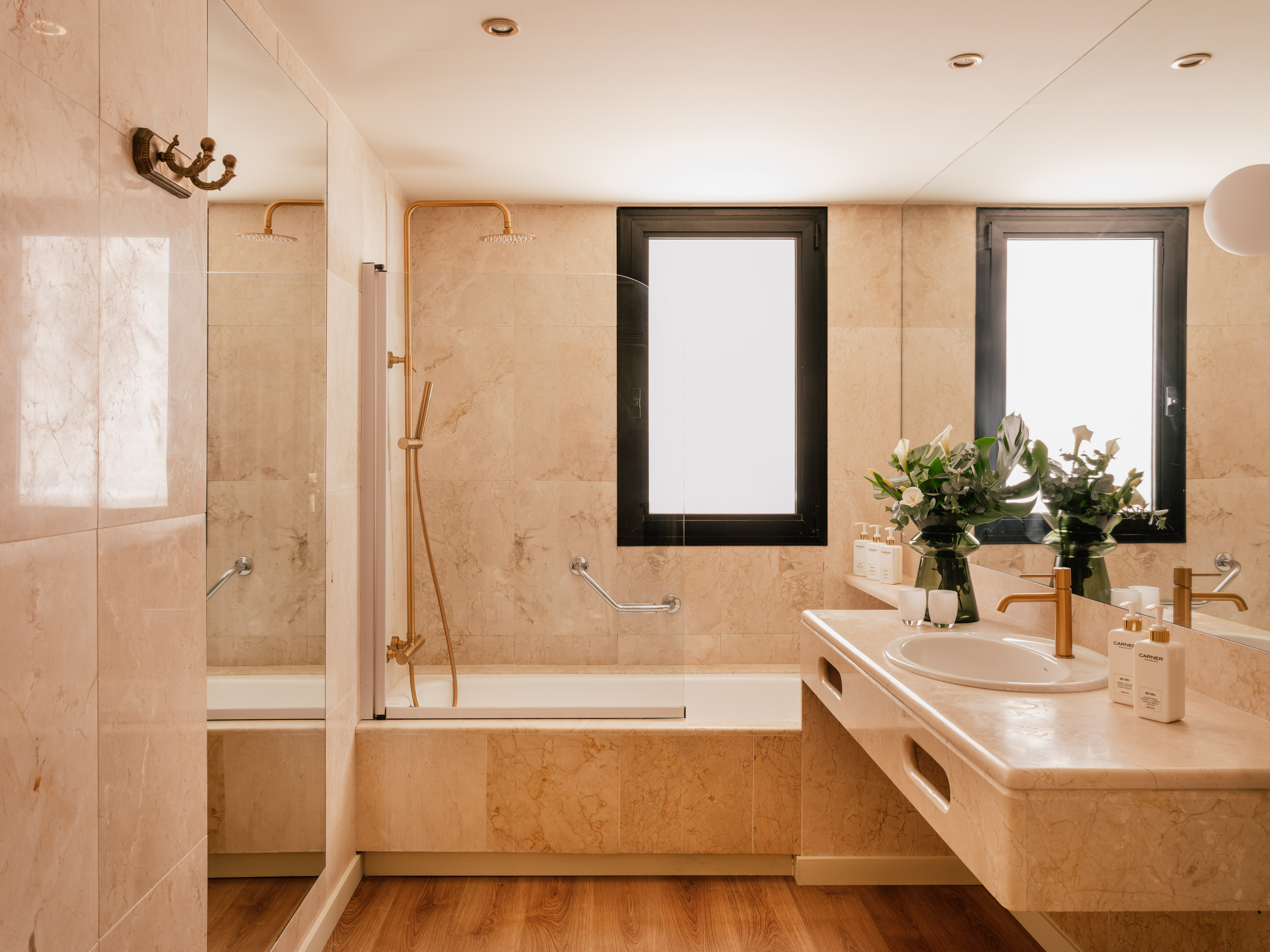 Modern marble bathroom with gold shower, bathtub, vanity, and wood floor.