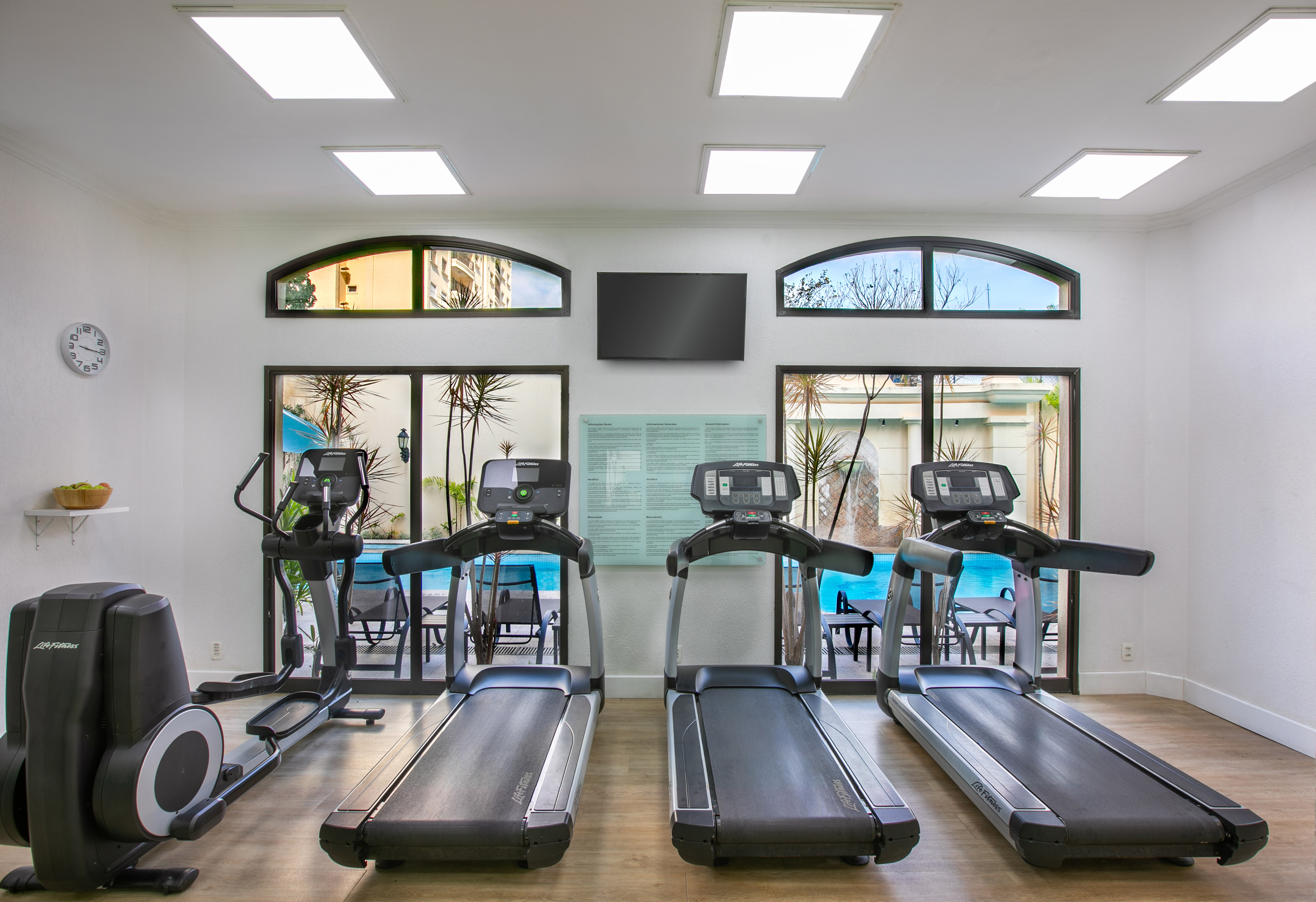 Modern gym with treadmills, elliptical, and pool view windows.
