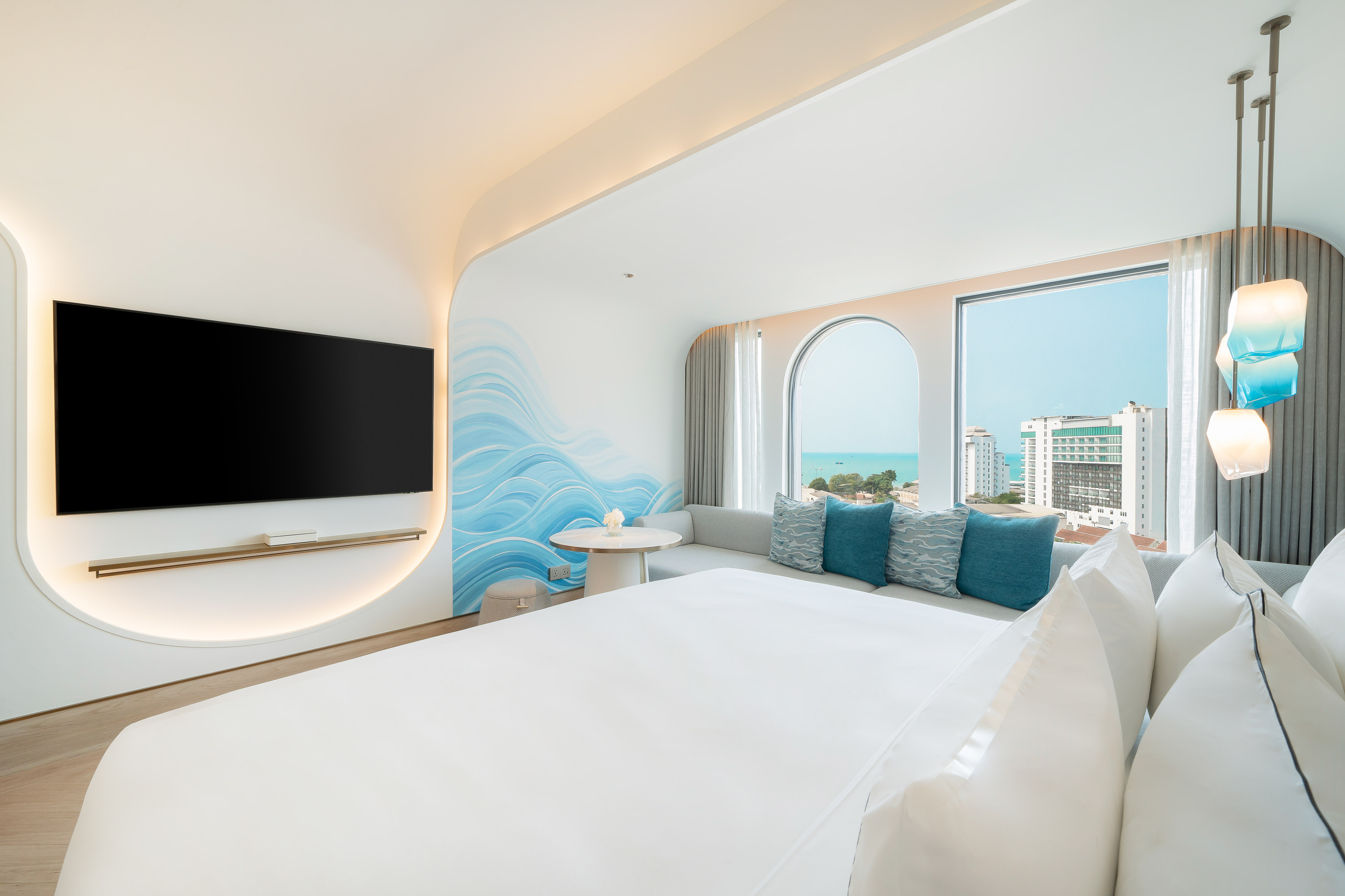 Modern hotel bedroom, ocean view, blue wave wall, large bed, and sofa.