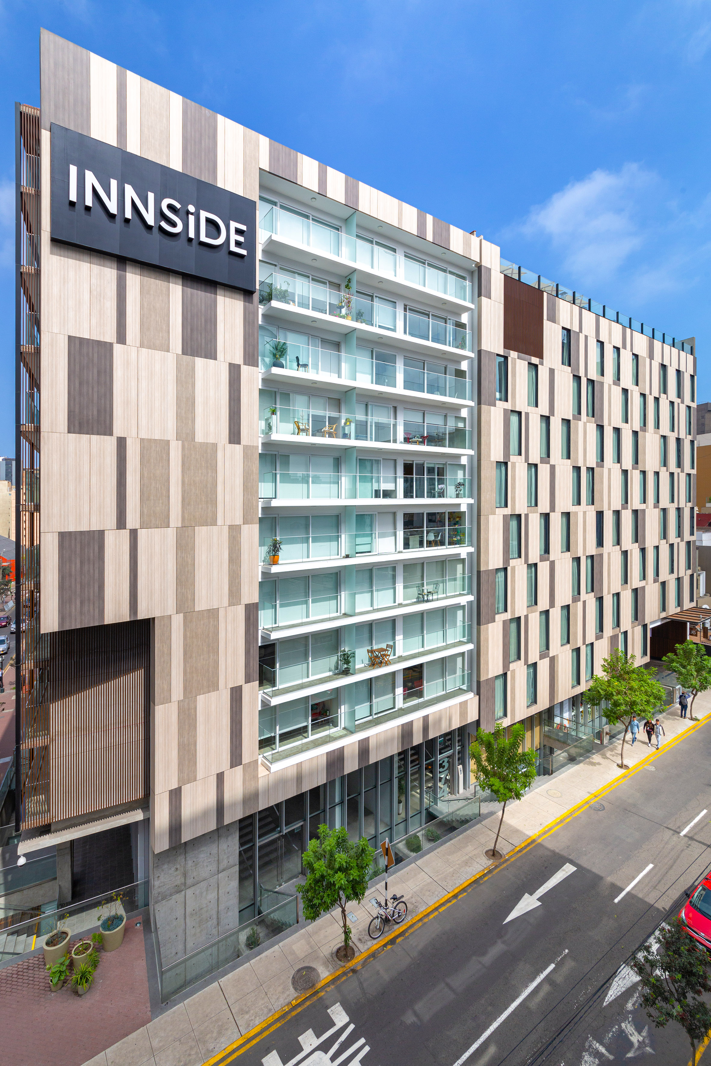 INNSIDE hotel with modern wood panel facade, glass balconies, and urban street view.