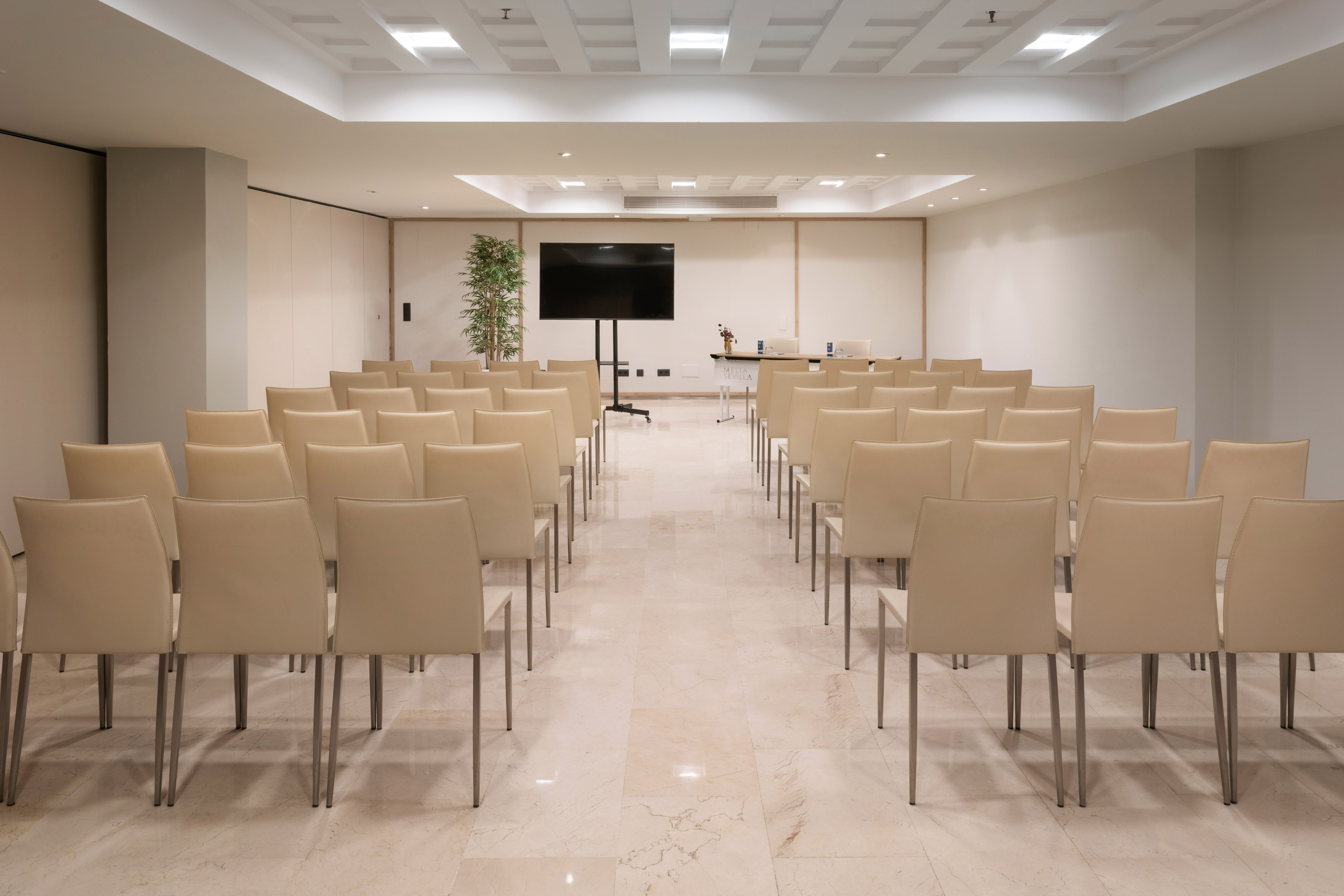 Modern empty meeting room with rows of cream chairs, large screen, and marble floor.