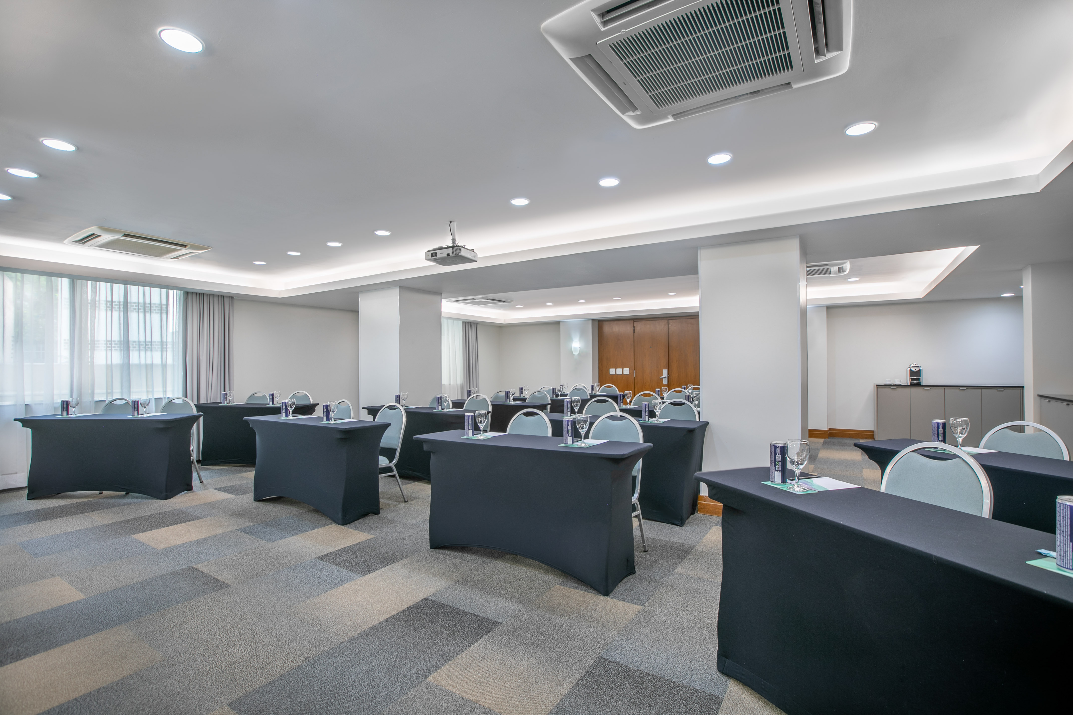 Modern meeting room with black tables, chairs, projector, patterned carpet.
