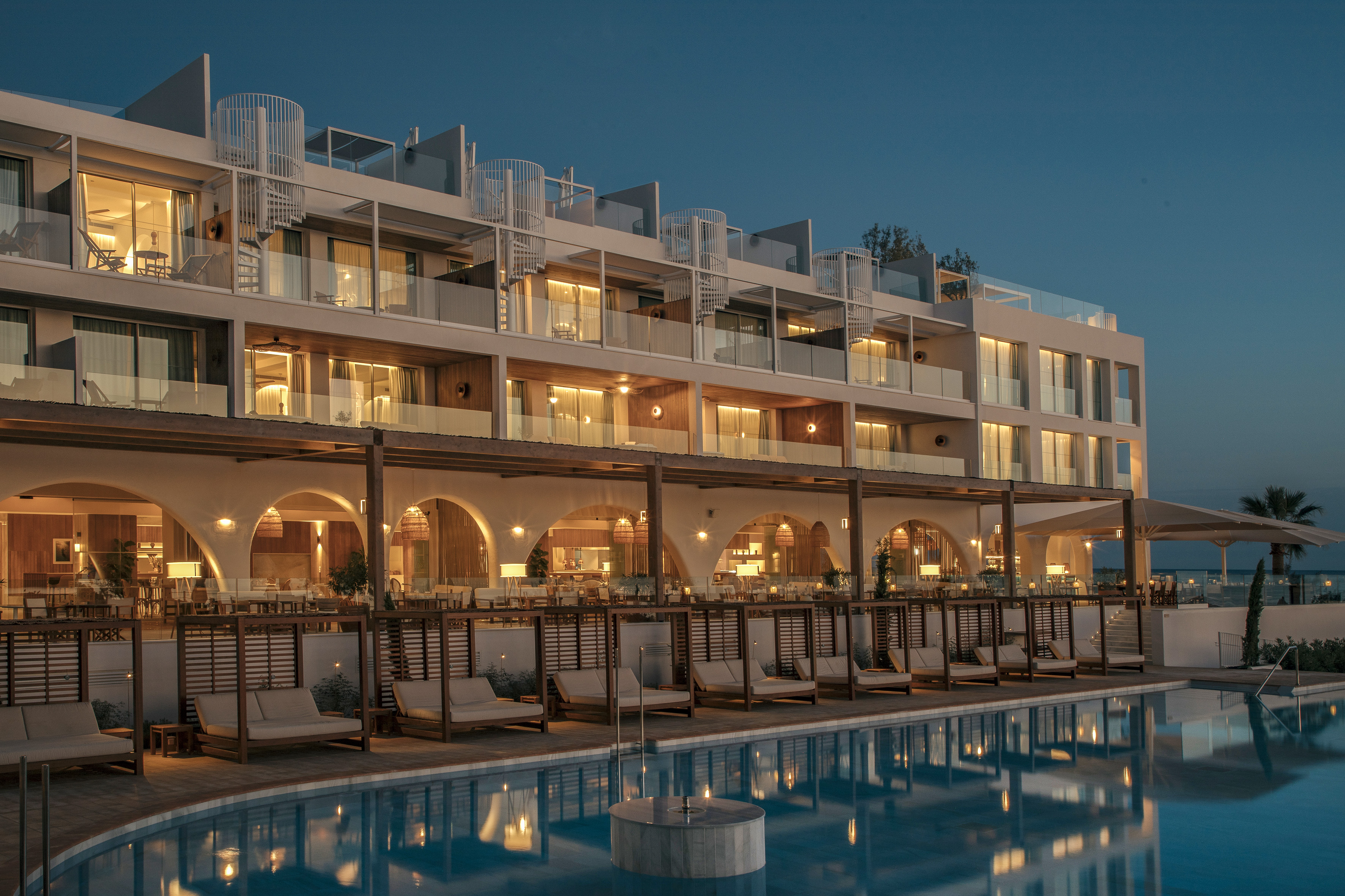 Luxury resort with illuminated pool, patio dining, and modern rooms at dusk.