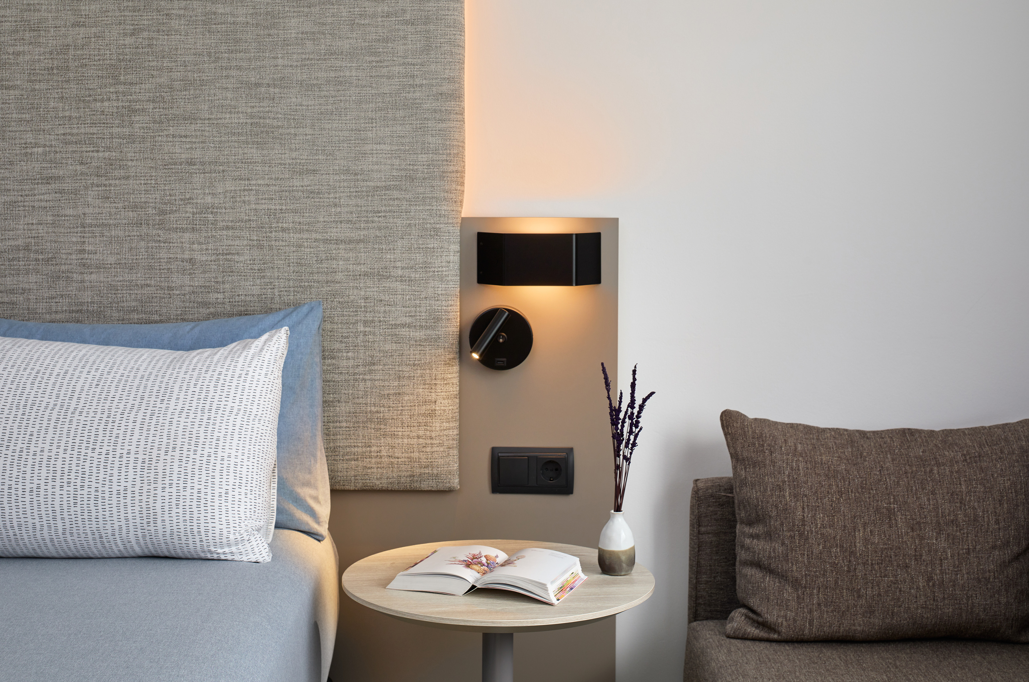 Modern bedroom nightstand, reading lamps, open book, and lavender decor.