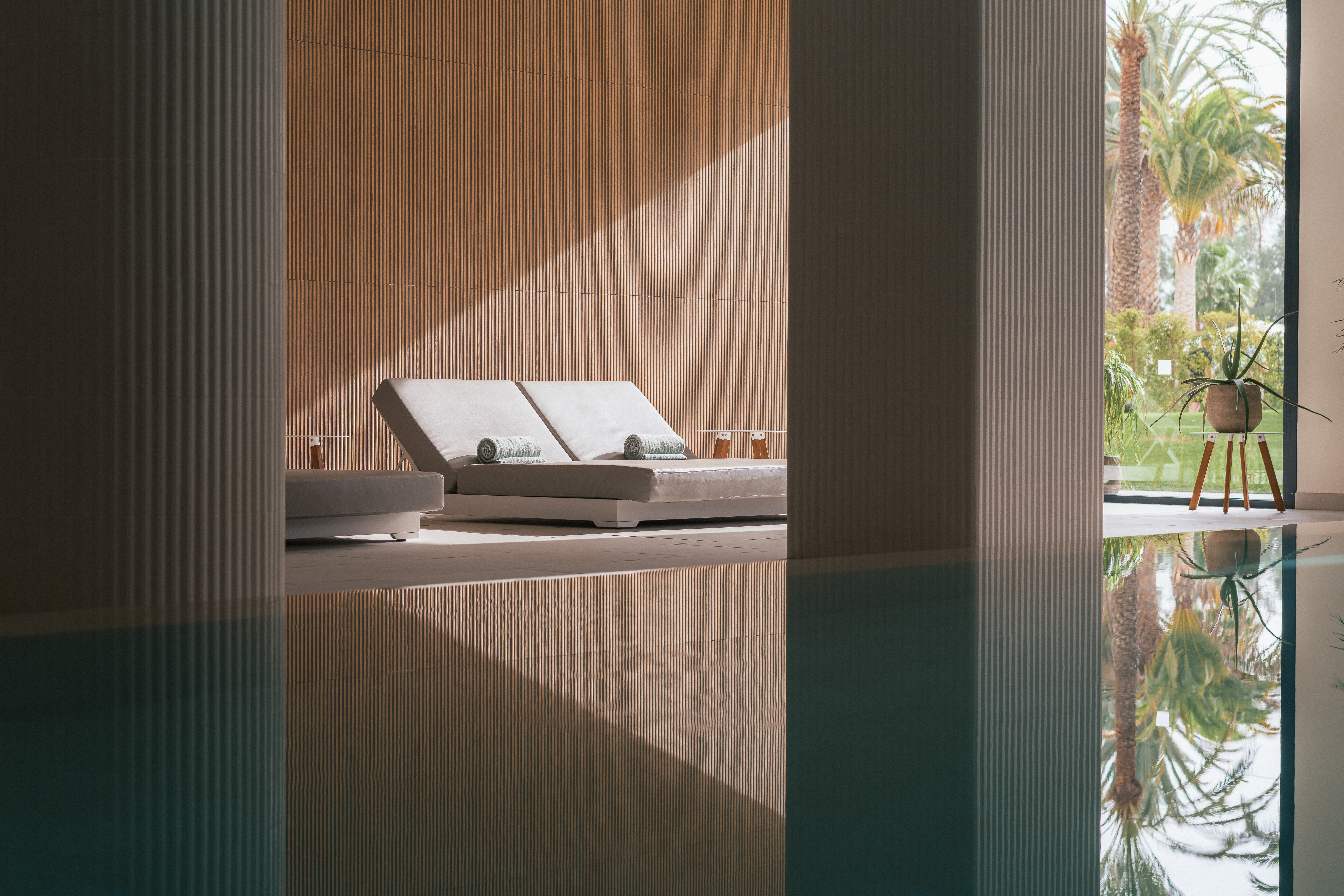 Indoor luxury pool with modern daybeds, wooden accents, and tropical views.