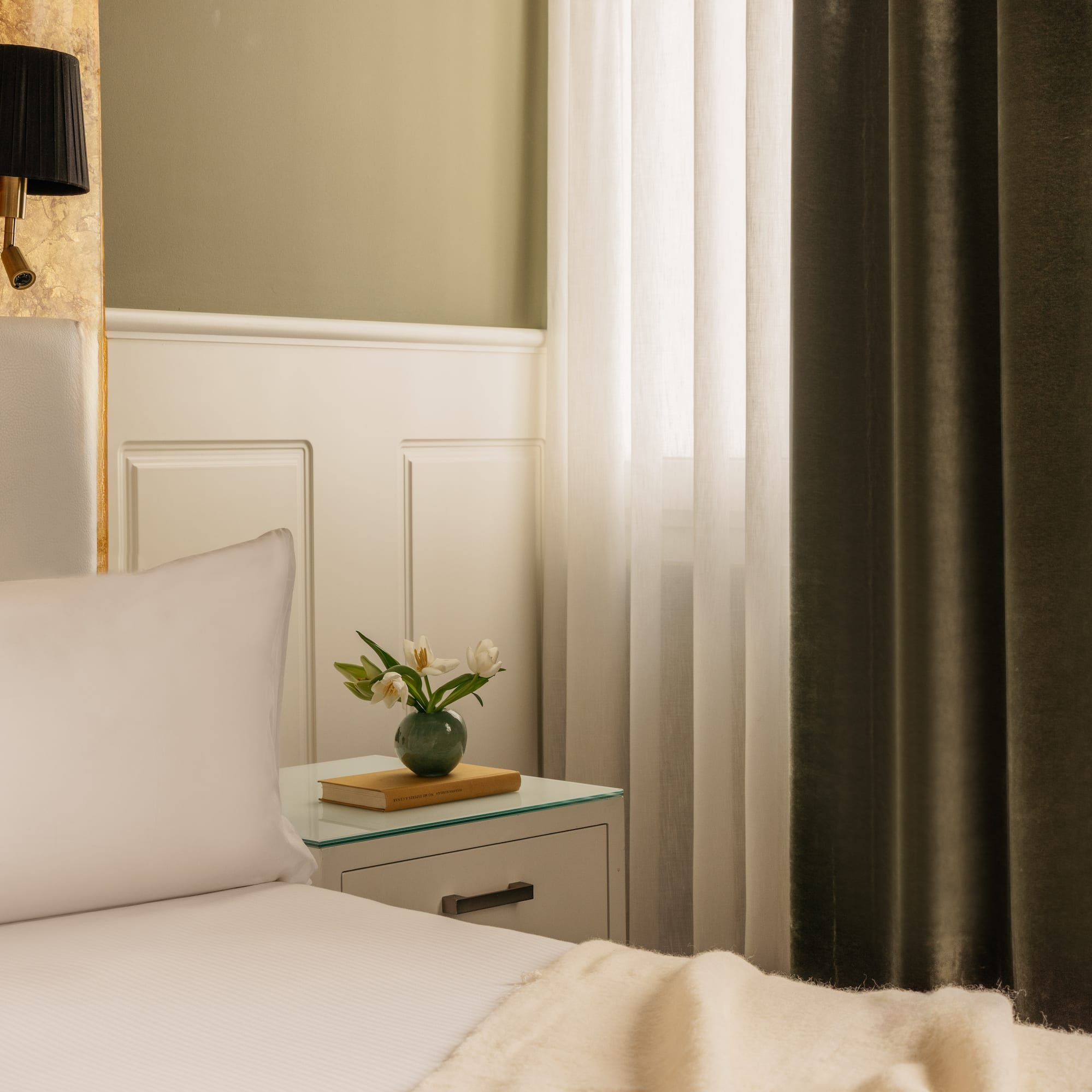 a bed with white sheets and a vase of flowers on a nightstand