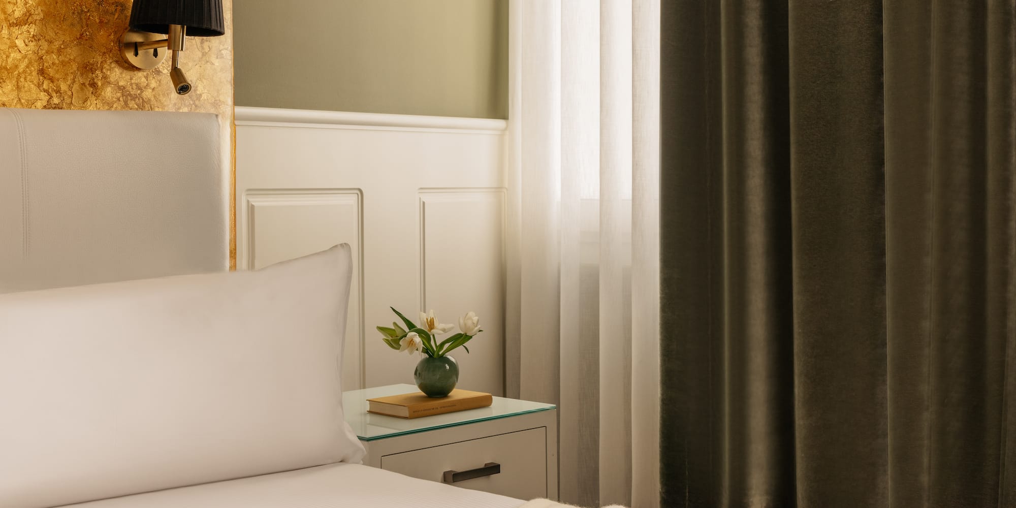a bed with white sheets and a vase of flowers on a nightstand
