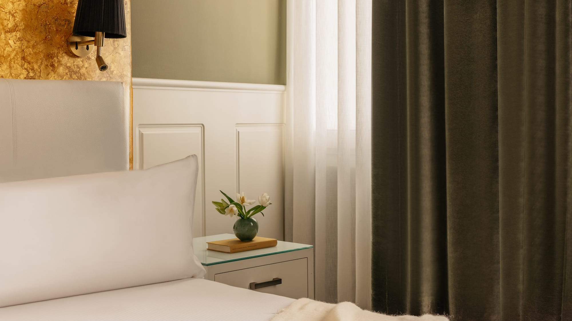 a bed with white sheets and a vase of flowers on a nightstand