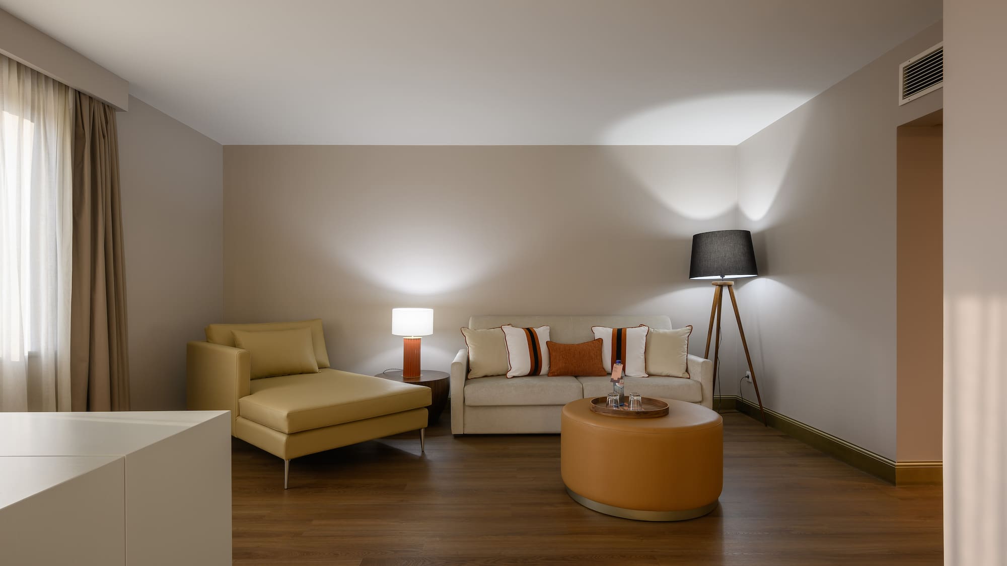 Modern living room with a light sofa, tan chaise lounge, and round ottoman.