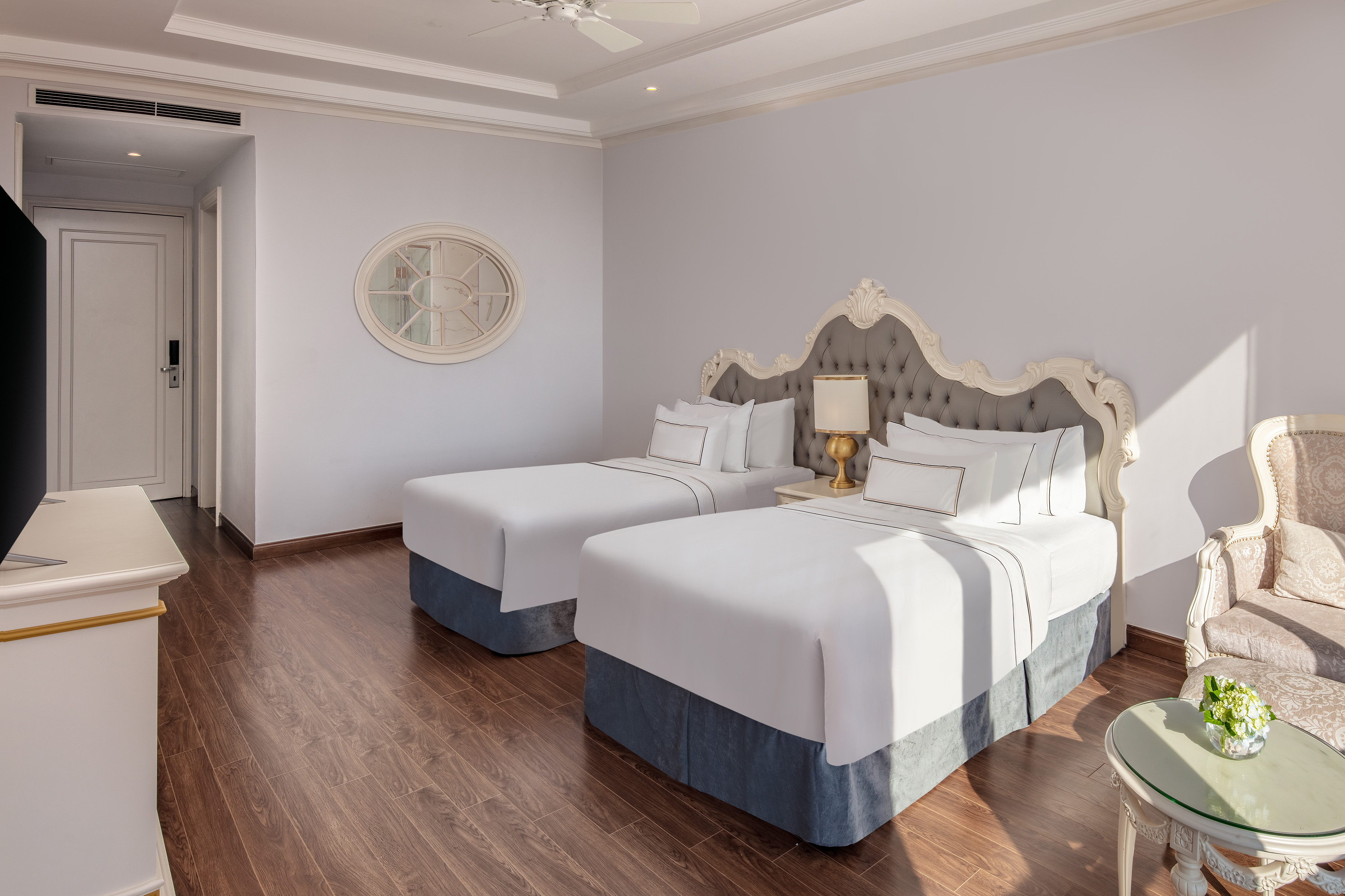 Elegant hotel room with two twin beds, ornate headboards, and wooden floor.