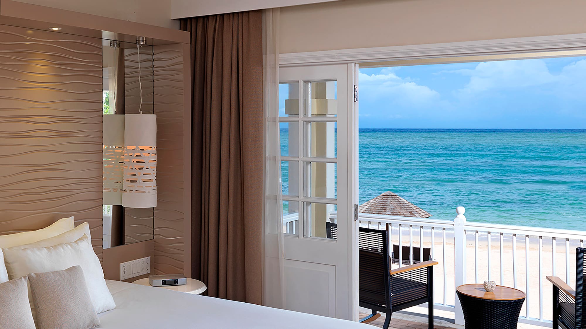 a room with a bed and chairs and a balcony overlooking the ocean