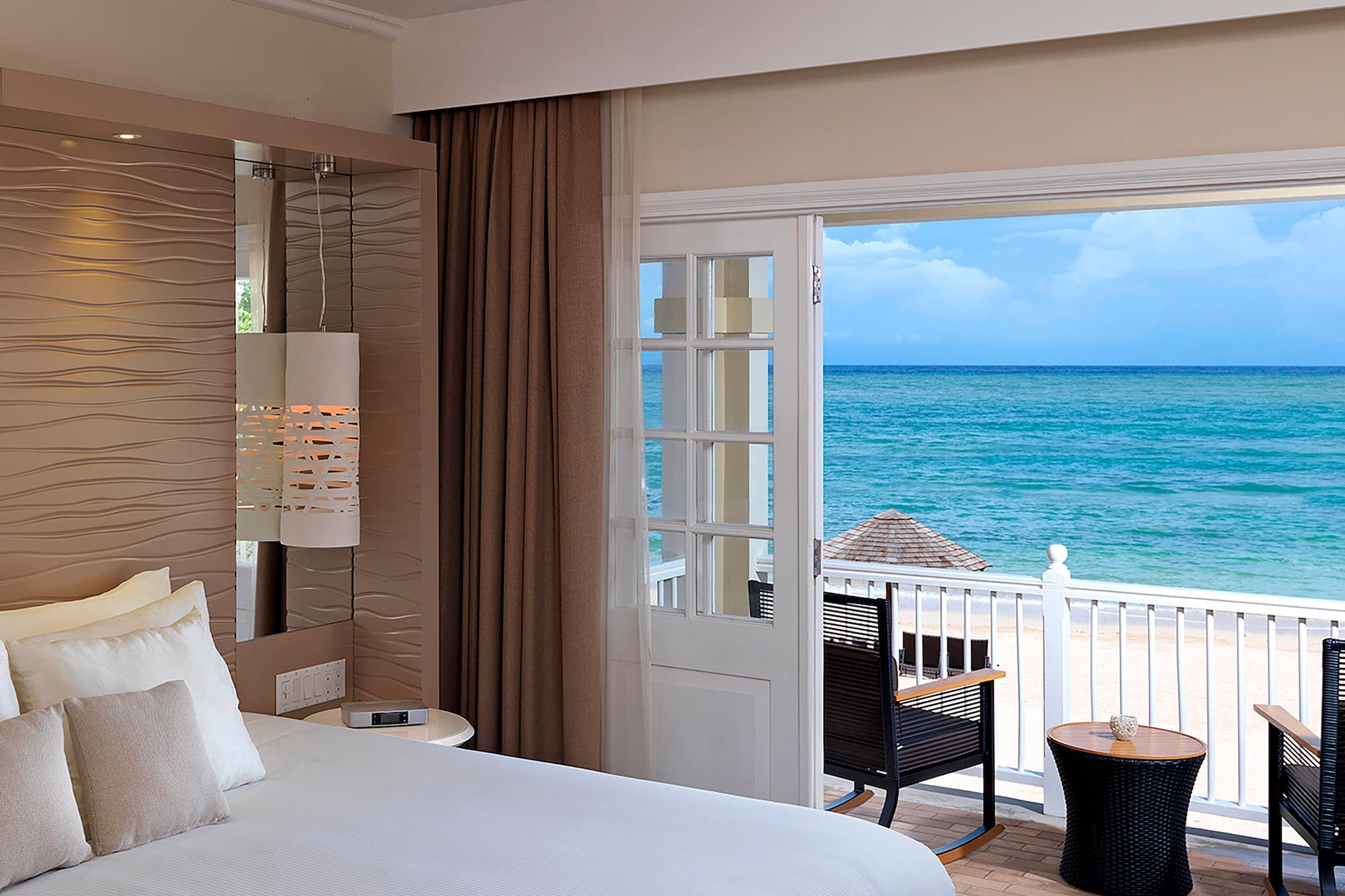 a room with a bed and chairs and a balcony overlooking the ocean