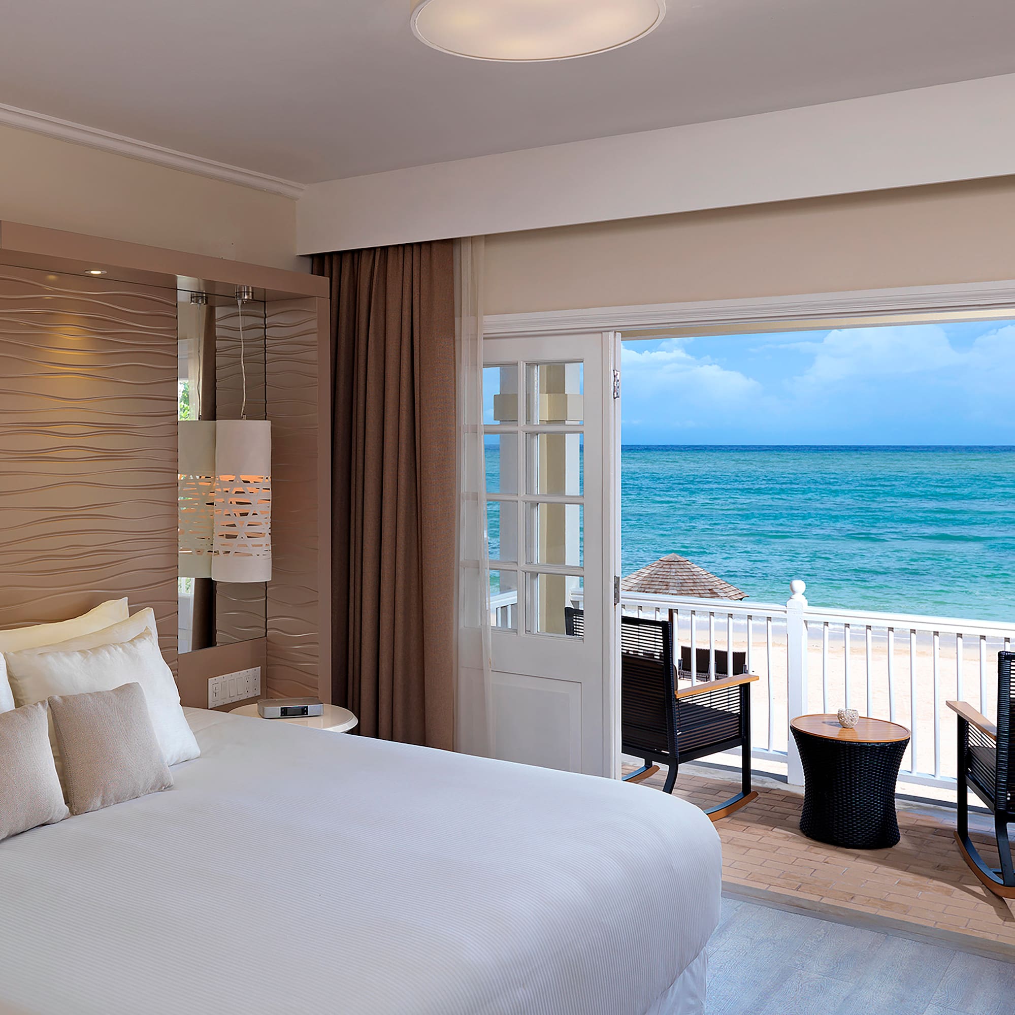 a room with a bed and chairs and a balcony overlooking the ocean