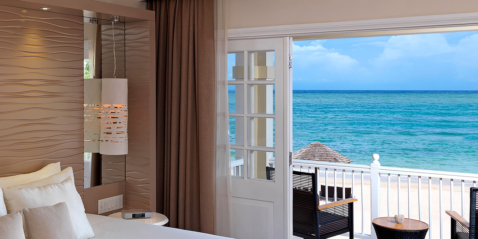 a room with a bed and chairs and a balcony overlooking the ocean