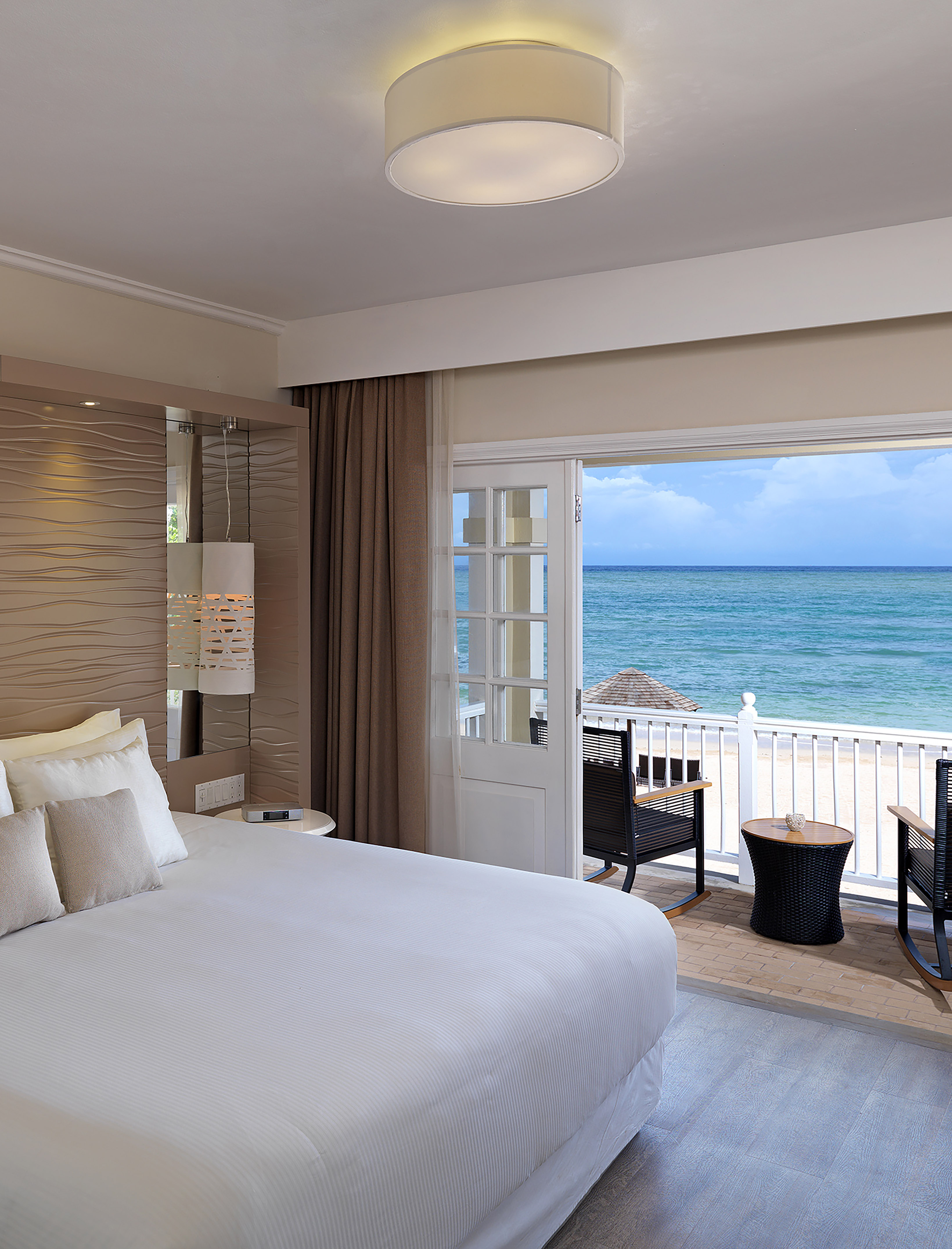 a room with a bed and chairs and a balcony overlooking the ocean