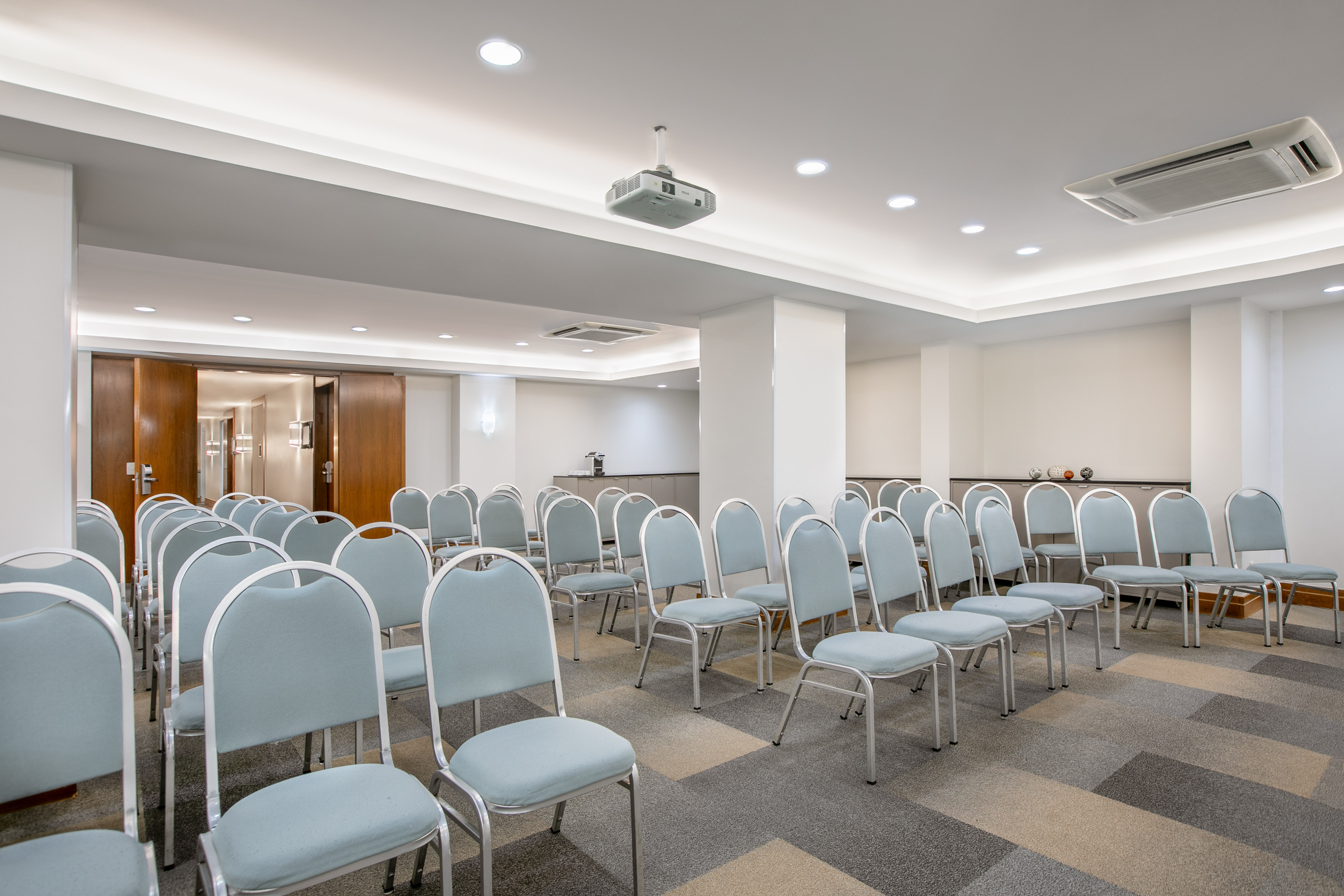 Modern conference room with blue chairs, ceiling projector, and patterned carpet.