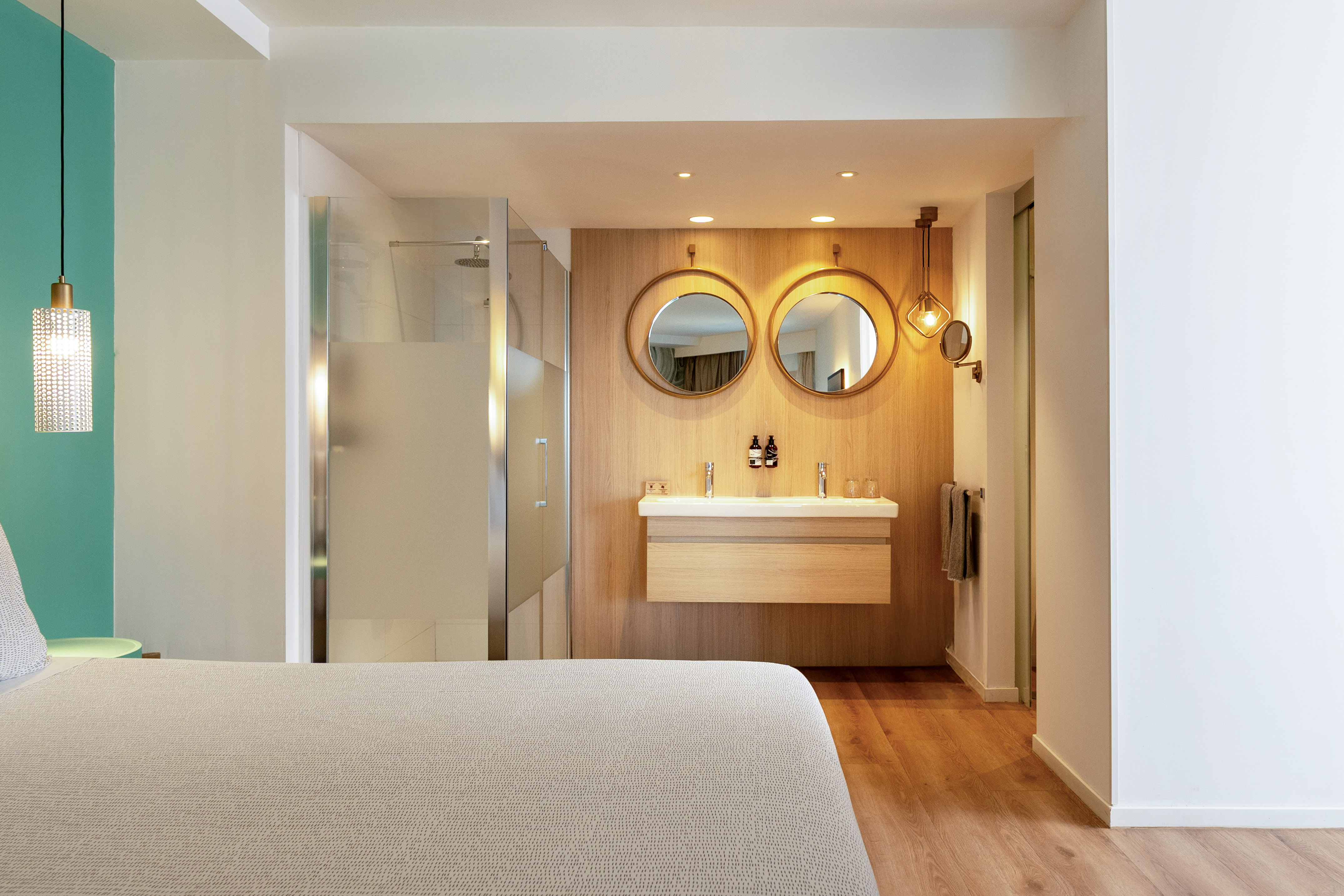Open-concept hotel bathroom with wood vanity, double mirrors, and glass shower.