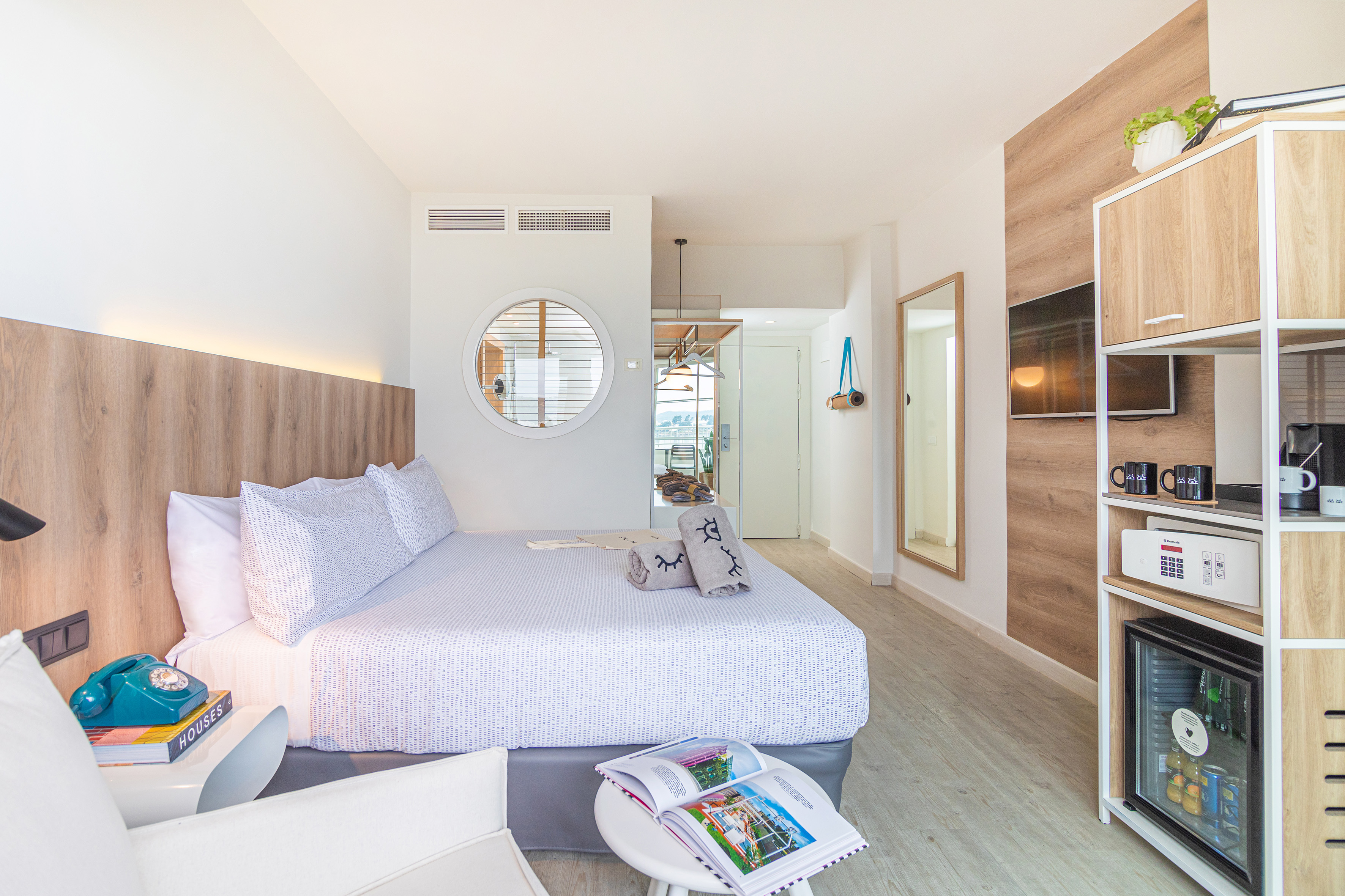 Modern hotel room with bed, wooden decor, TV, and mini-bar.