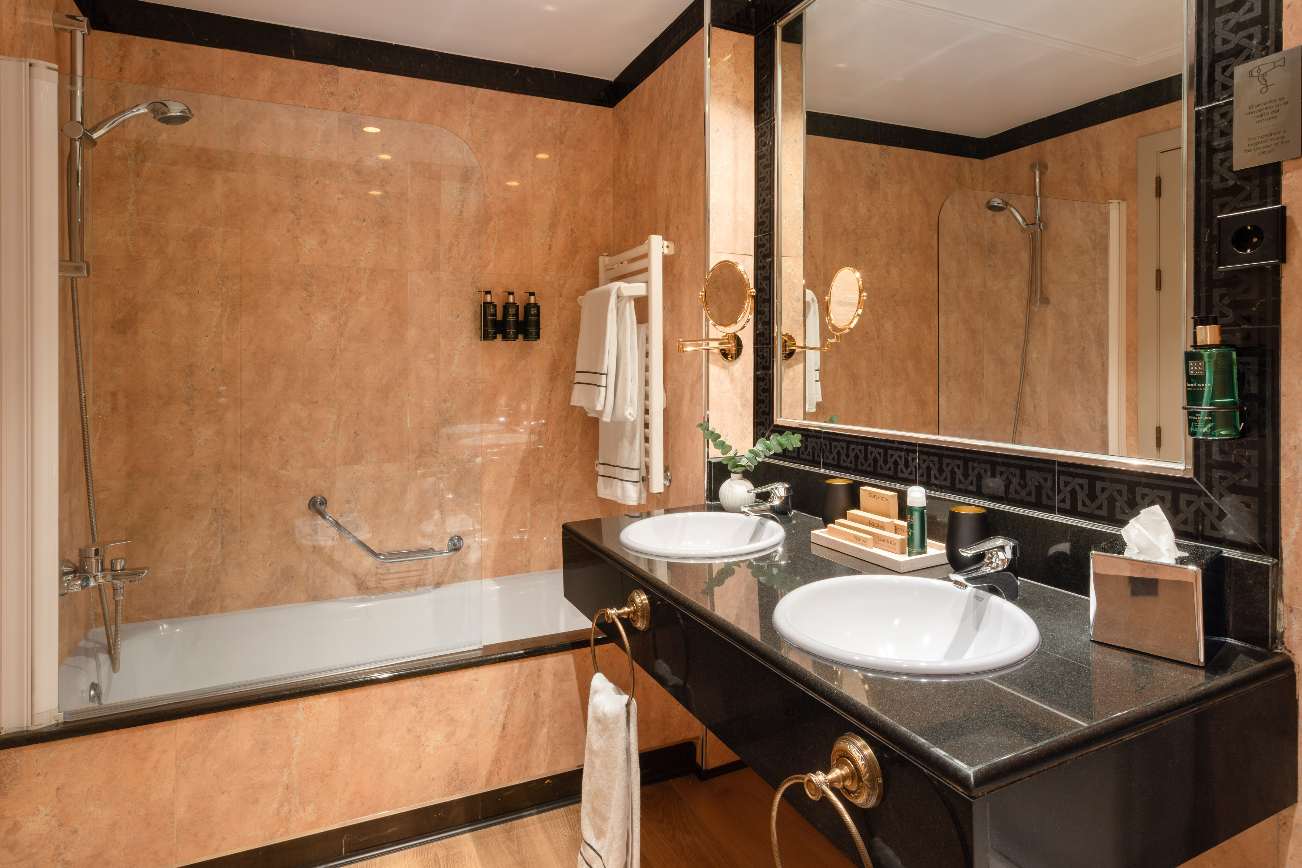 Luxury hotel bathroom with double vanity, marble walls, and bathtub shower.