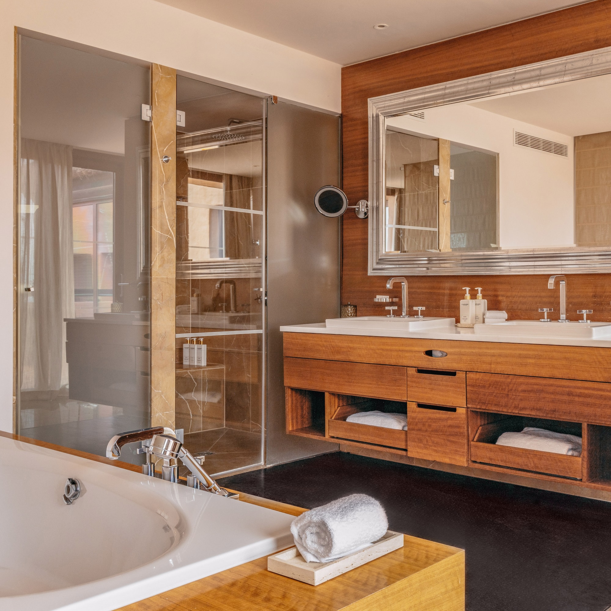 Modern luxury bathroom with bathtub, double vanity, wood accents, and glass shower.