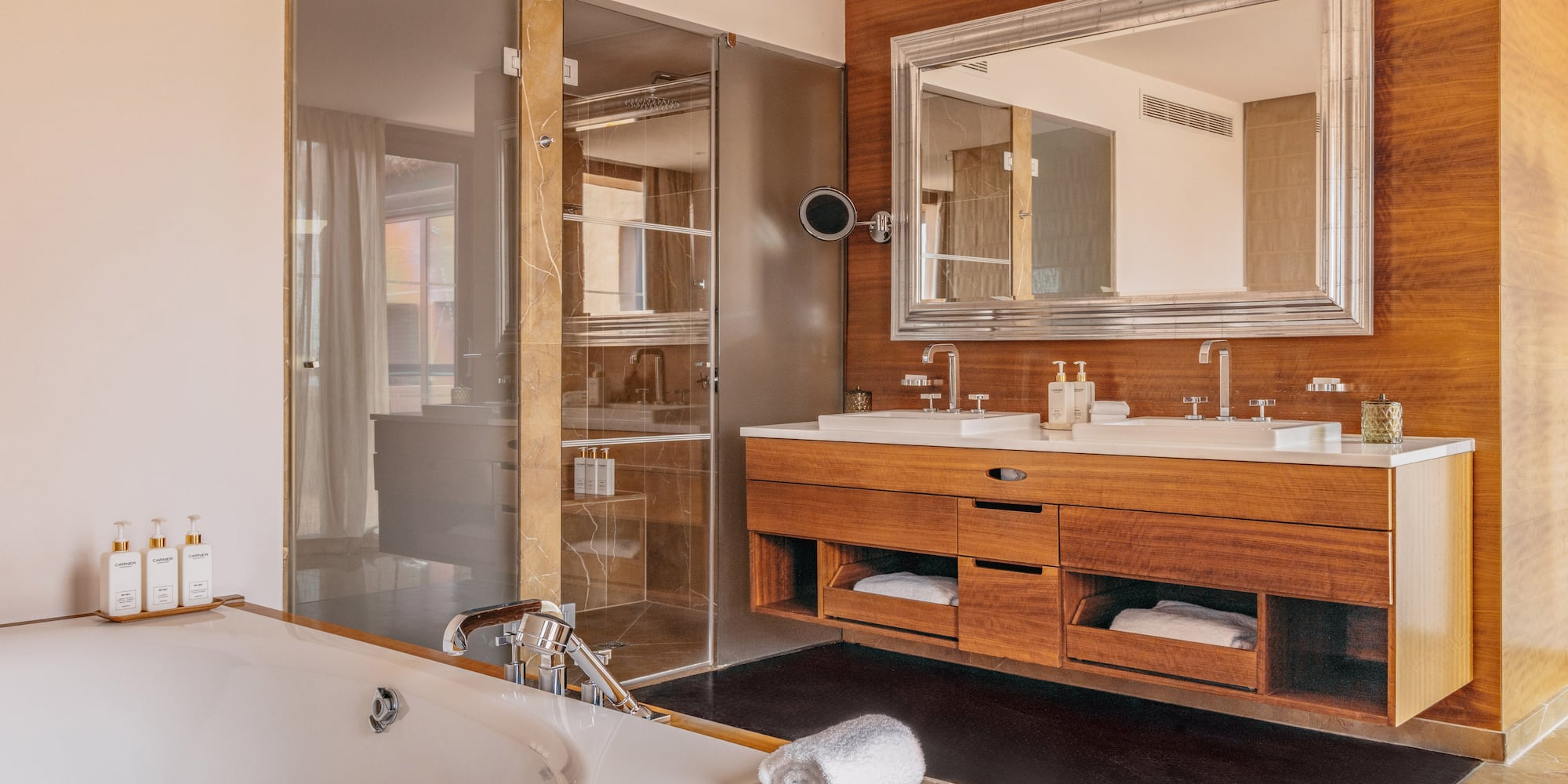 Modern luxury bathroom with bathtub, double vanity, wood accents, and glass shower.