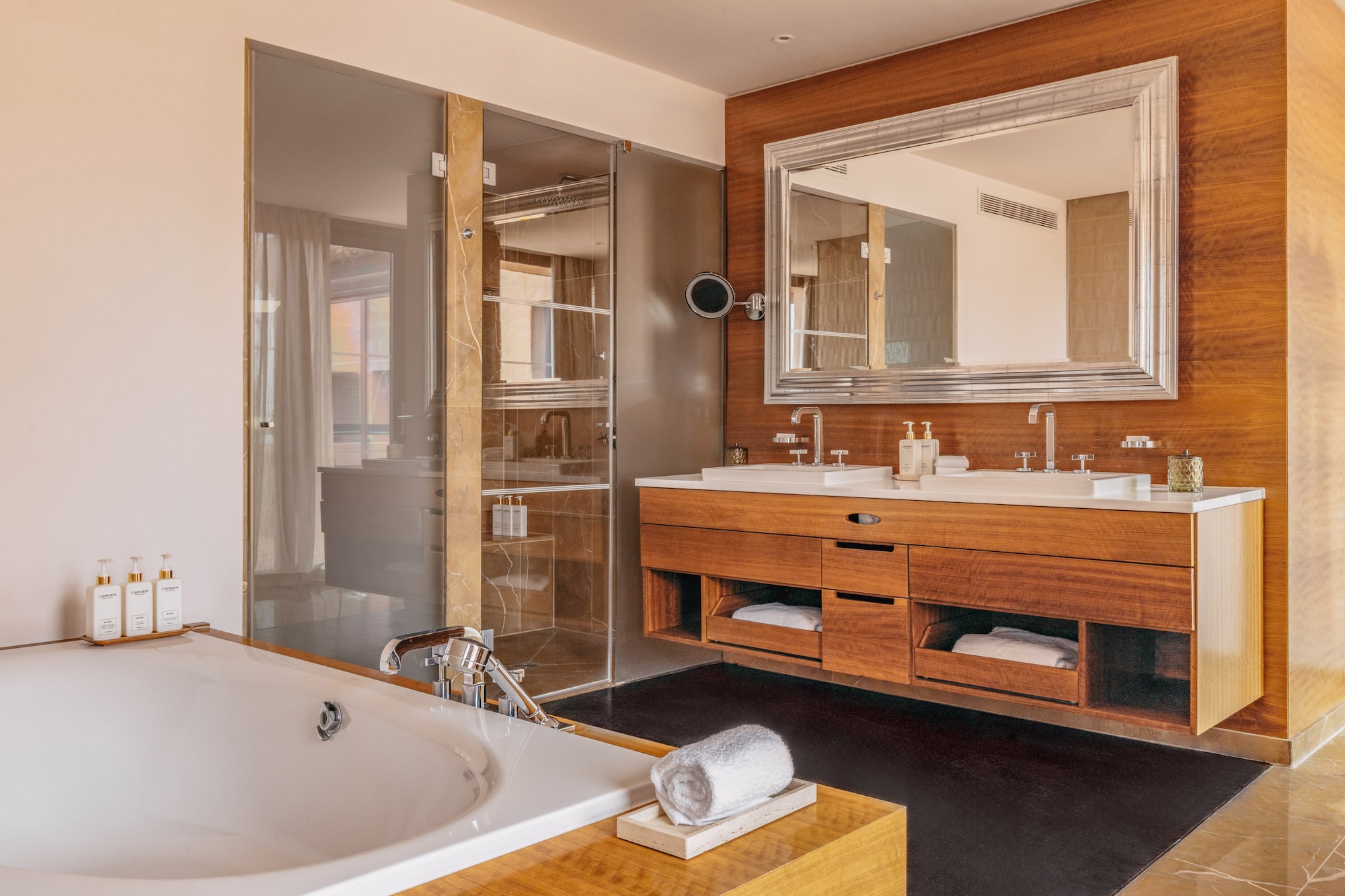 Modern luxury bathroom with bathtub, double vanity, wood accents, and glass shower.