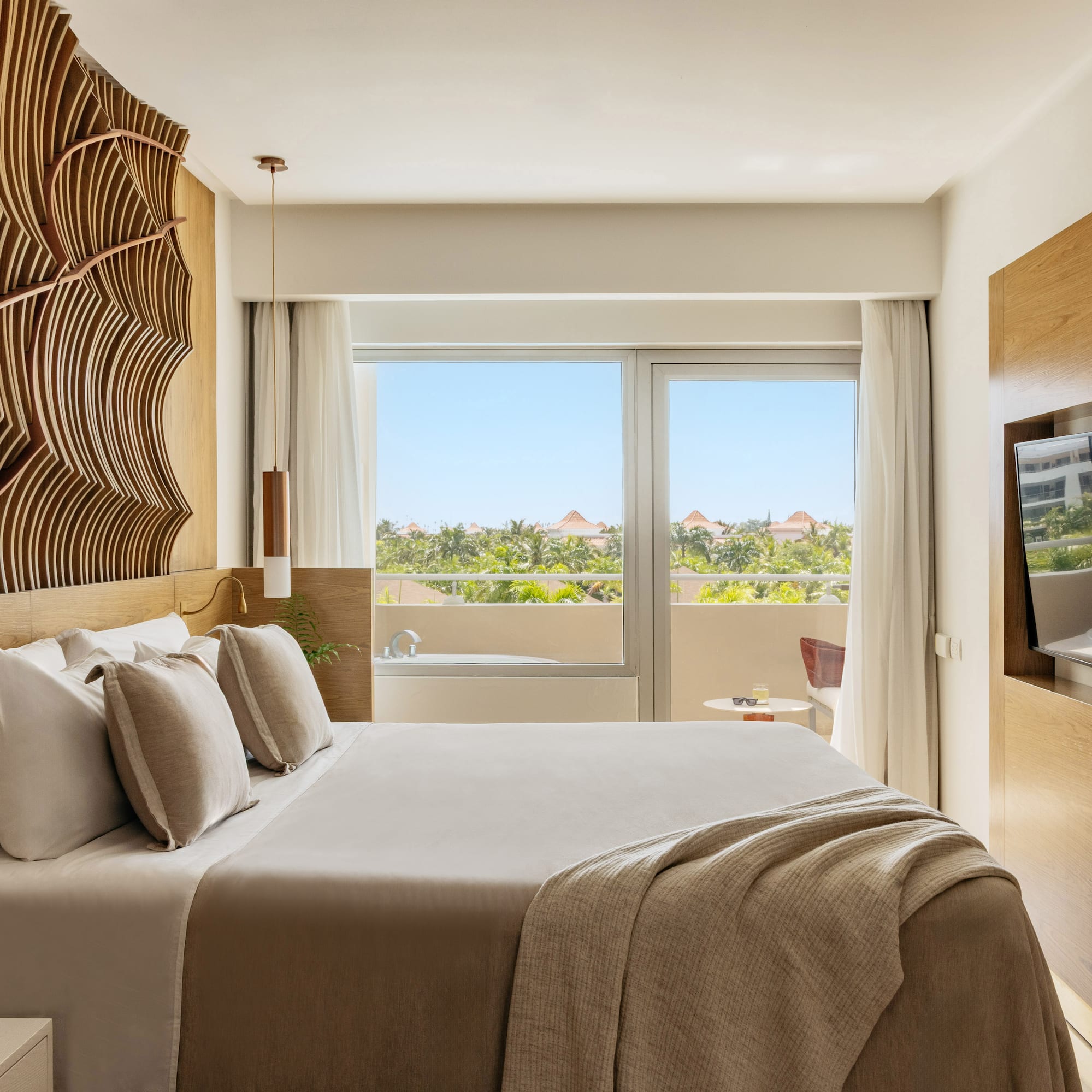 Luxury hotel room with king bed, wavy wooden headboard, tropical view.