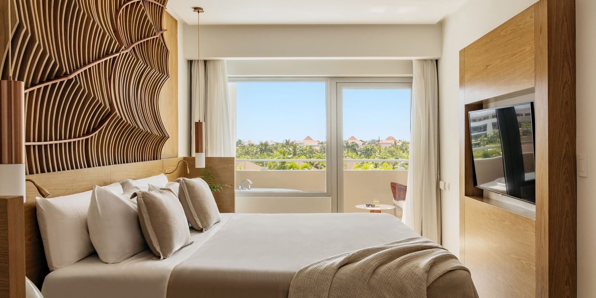 Luxury hotel room with king bed, wavy wooden headboard, tropical view.