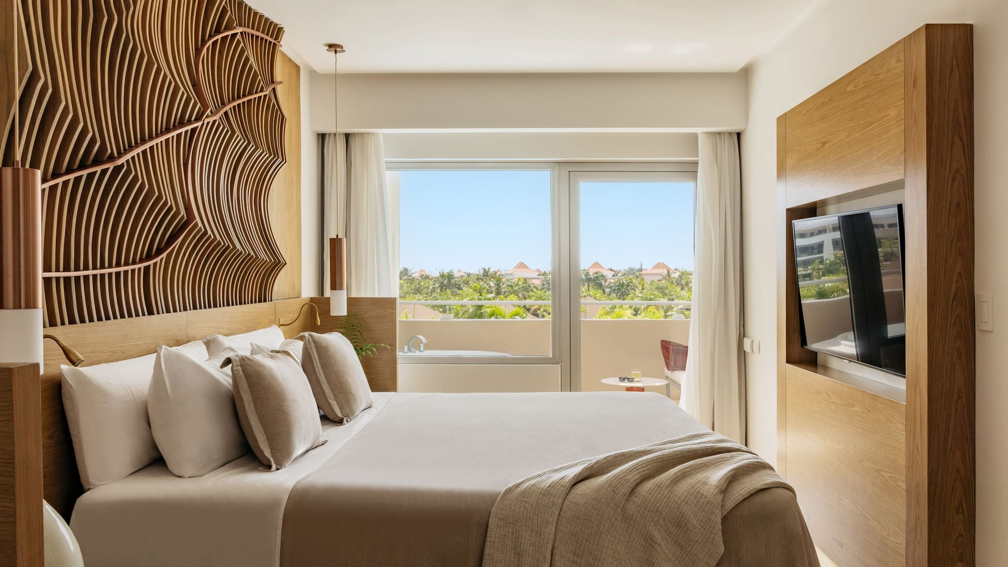 Luxury hotel room with king bed, wavy wooden headboard, tropical view.